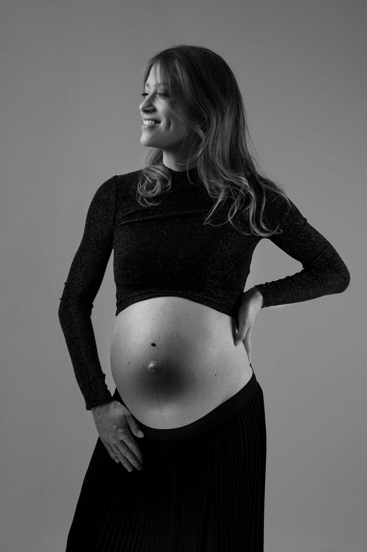 Black and white portrait of a smiling pregnant woman in a black crop top showing her baby bump.