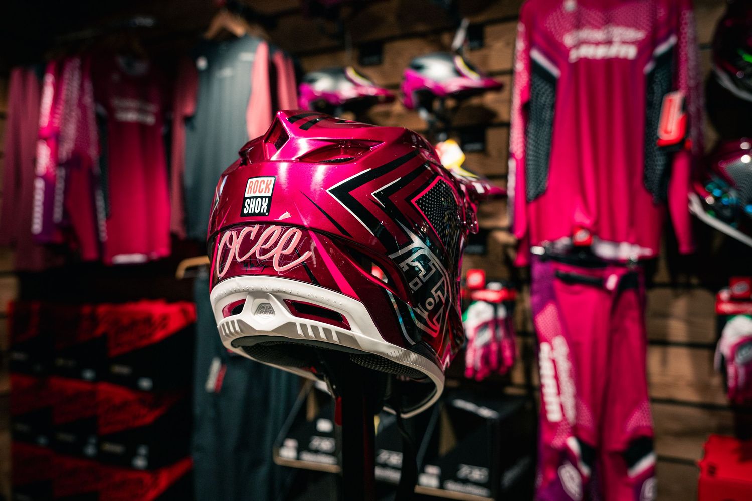 Pink motocross helmet with bold graphic design displayed in a motorsports gear shop with matching pink jerseys.