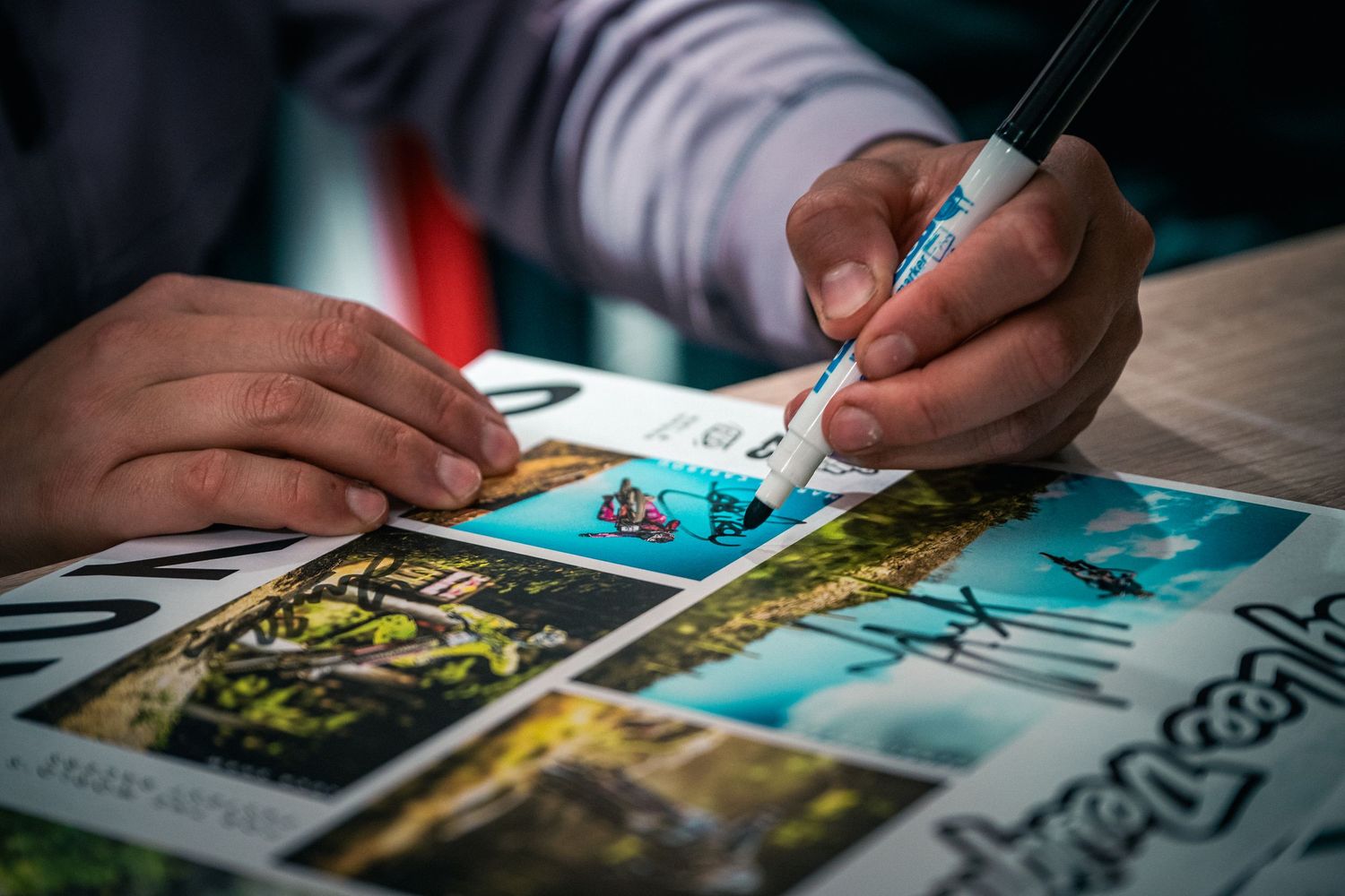 Close-up of hands carefully drawing and writing on travel postcards with a fine-tip pen on a wooden table.