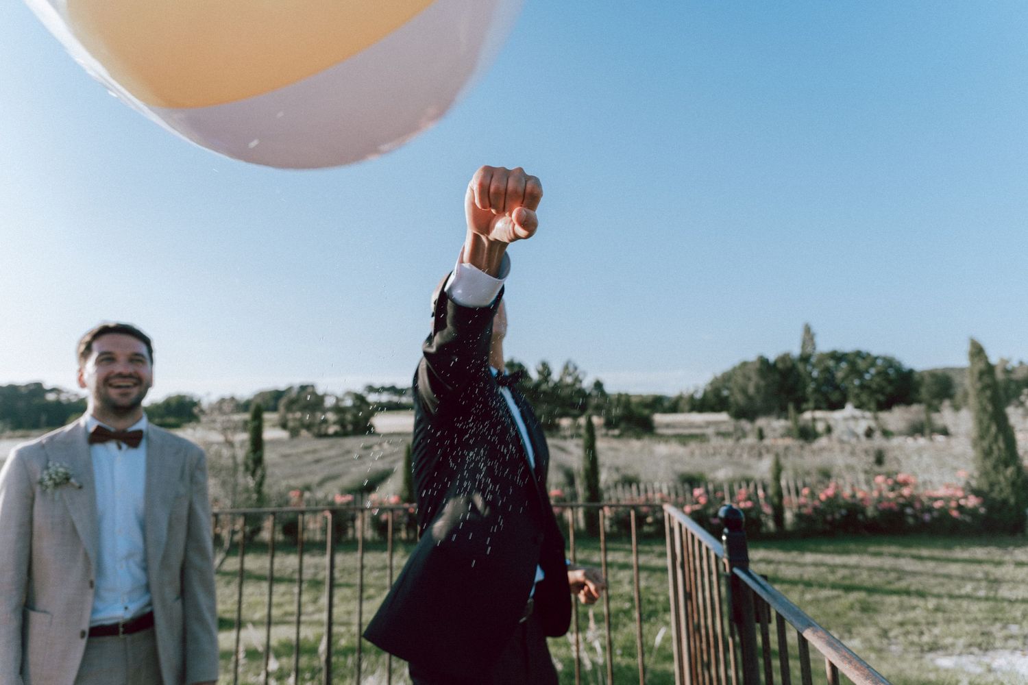 Groomsman releasing large balloon outdoors at sunny rustic wedding celebration venue.