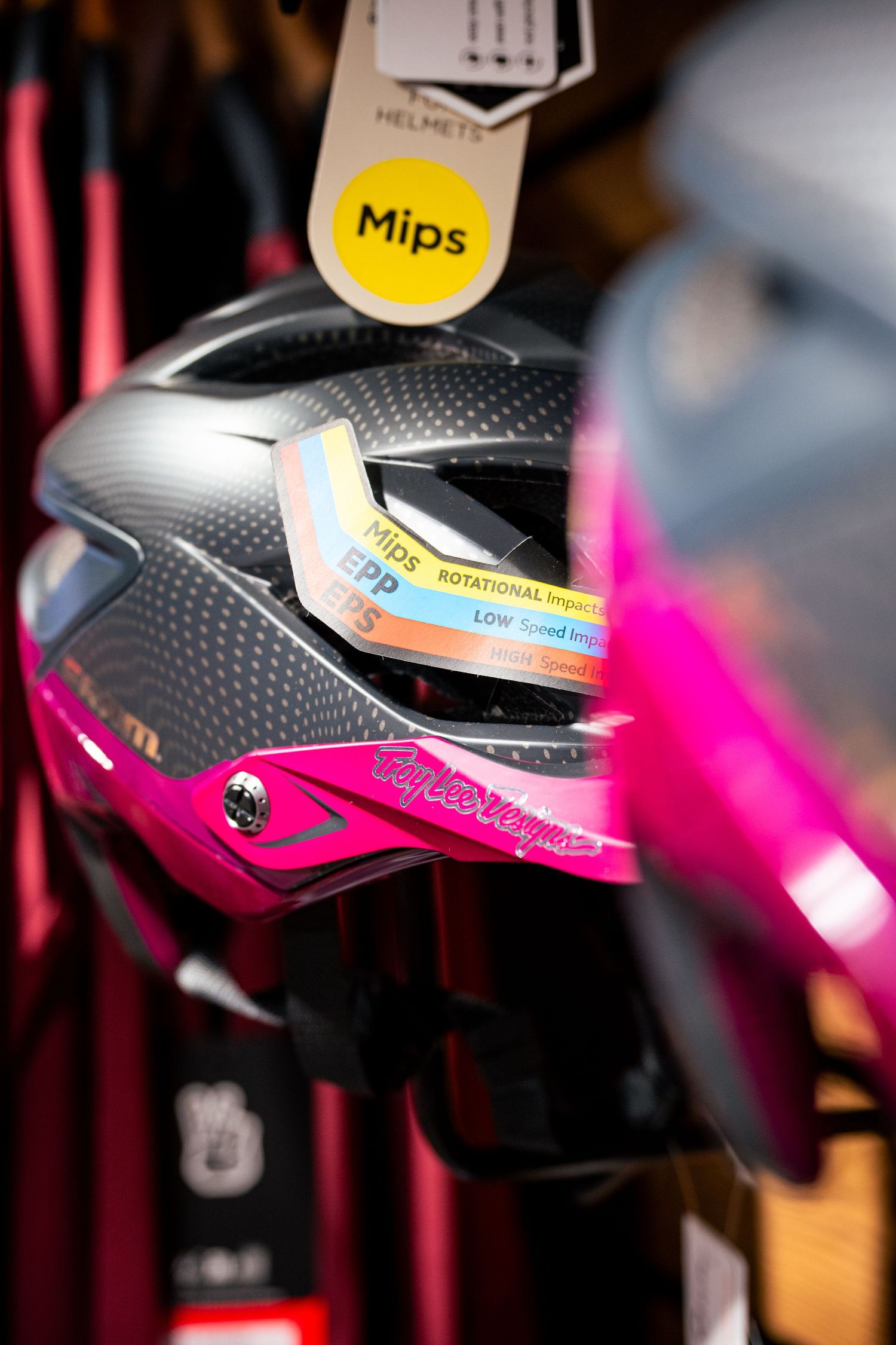 Pink and black Troy Lee Designs MIPS cycling helmet displayed on a store rack with safety technology labels.