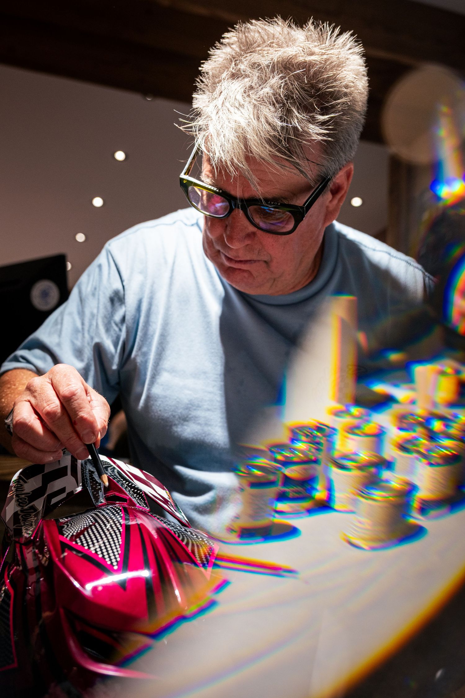 Artist with glasses carefully detailing a pink motocross helmet at a worktable.