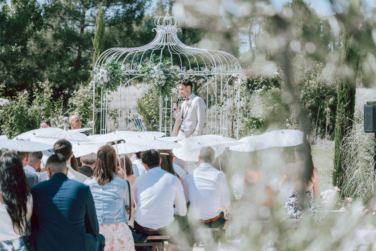 Officiant standing at white gazebo altar during romantic outdoor garden wedding ceremony.