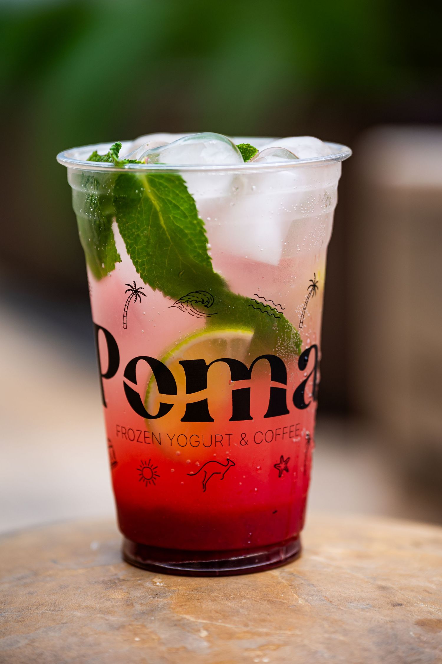 Poma Frozen Yogurt & Coffee red iced drink with mint leaves and lime in branded cup.