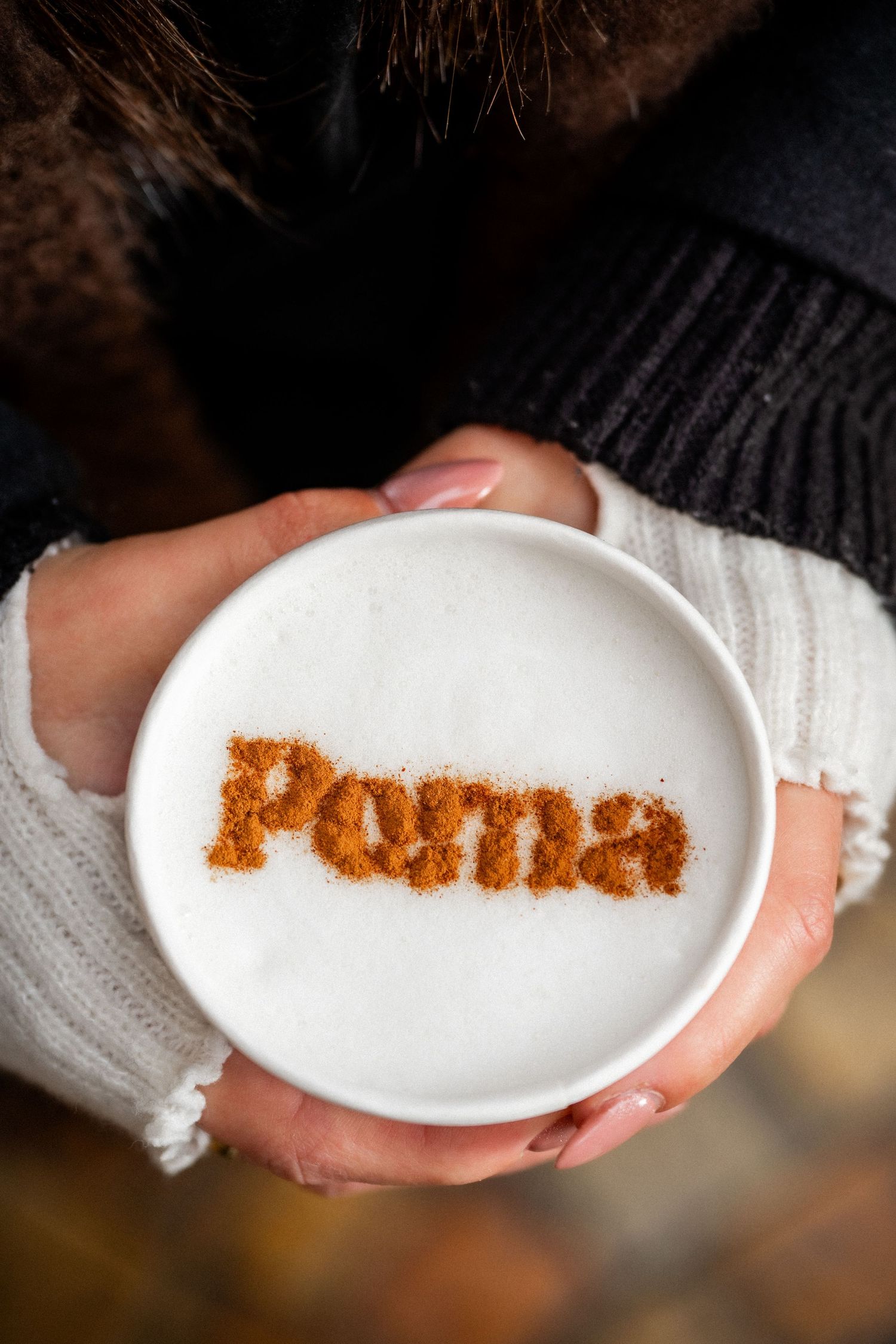 Overhead view of a latte with Poma spelled in cinnamon powder on creamy foam.