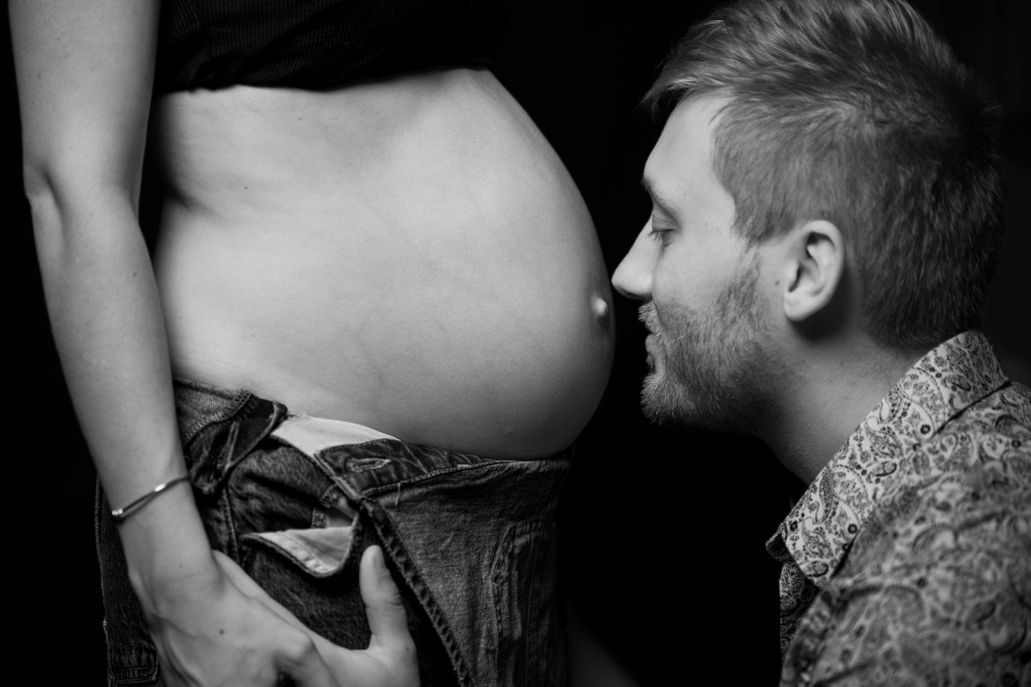 Man tenderly kissing pregnant woman's baby bump in intimate black and white maternity photograph.