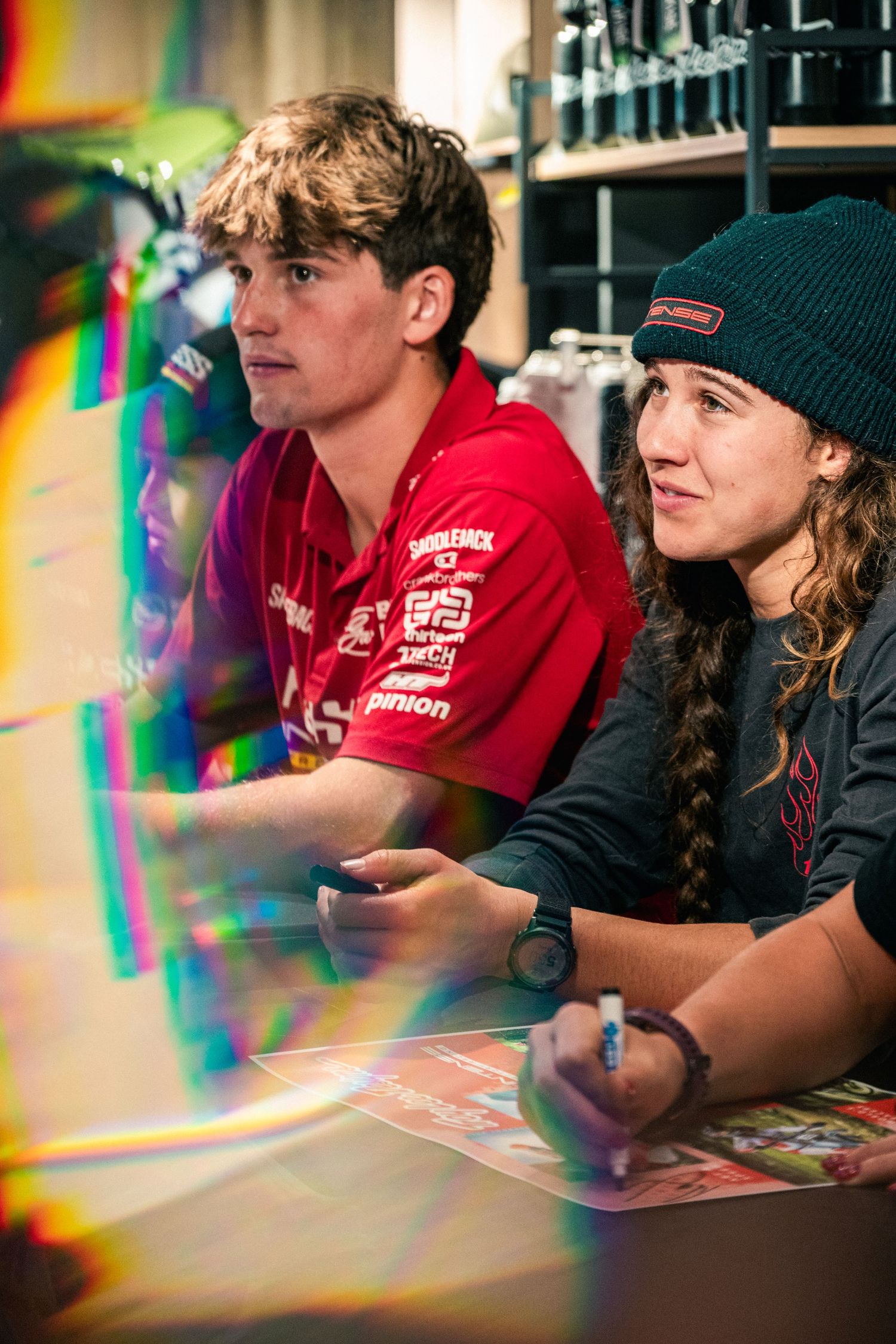 Two young people signing autographs at a gaming or sports event, wearing branded apparel.