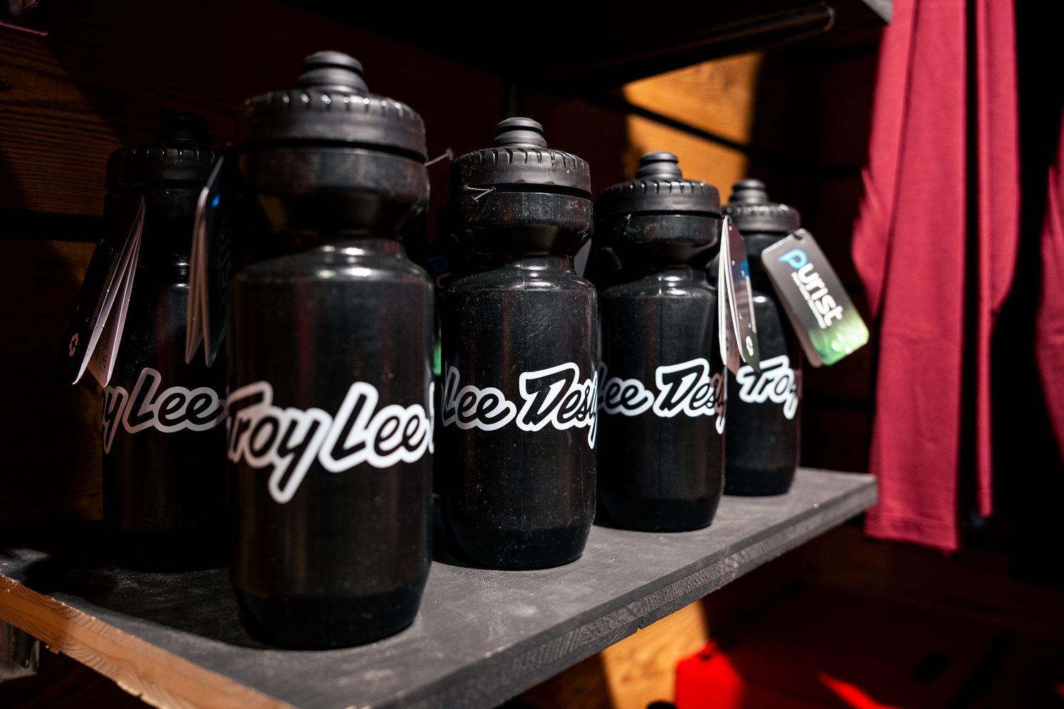 Row of black Troy Lee Designs water bottles displayed on a shelf in a dimly lit room.