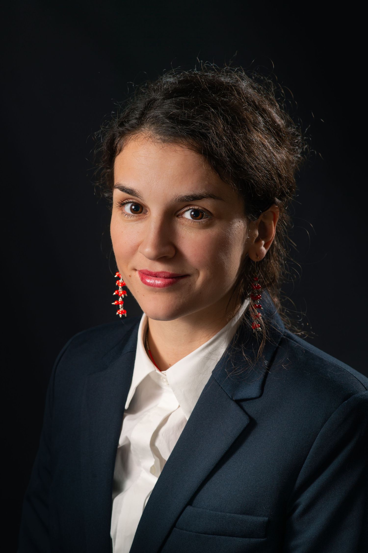 Professional woman in navy blazer with red drop earrings smiling in formal portrait.