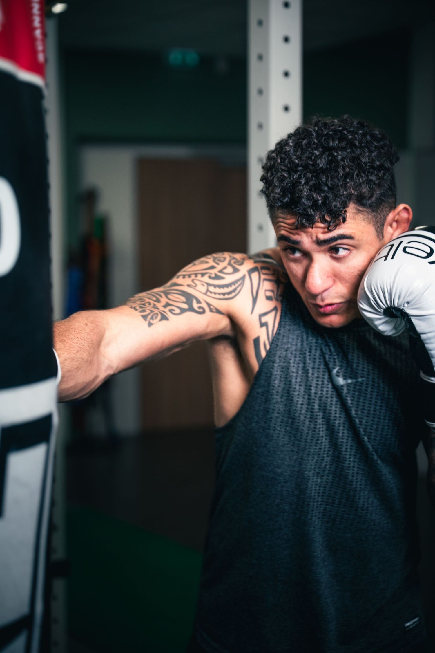 Tattooed male boxer throwing a punch at a heavy bag during training in a gym.