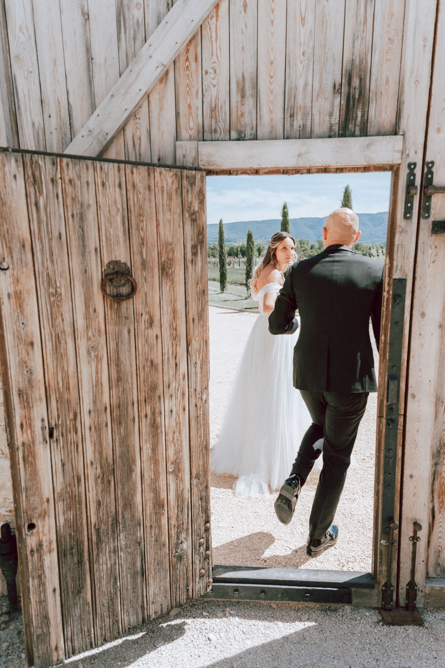 Bride and groom share a romantic moment framed by rustic wooden barn doors at outdoor wedding.