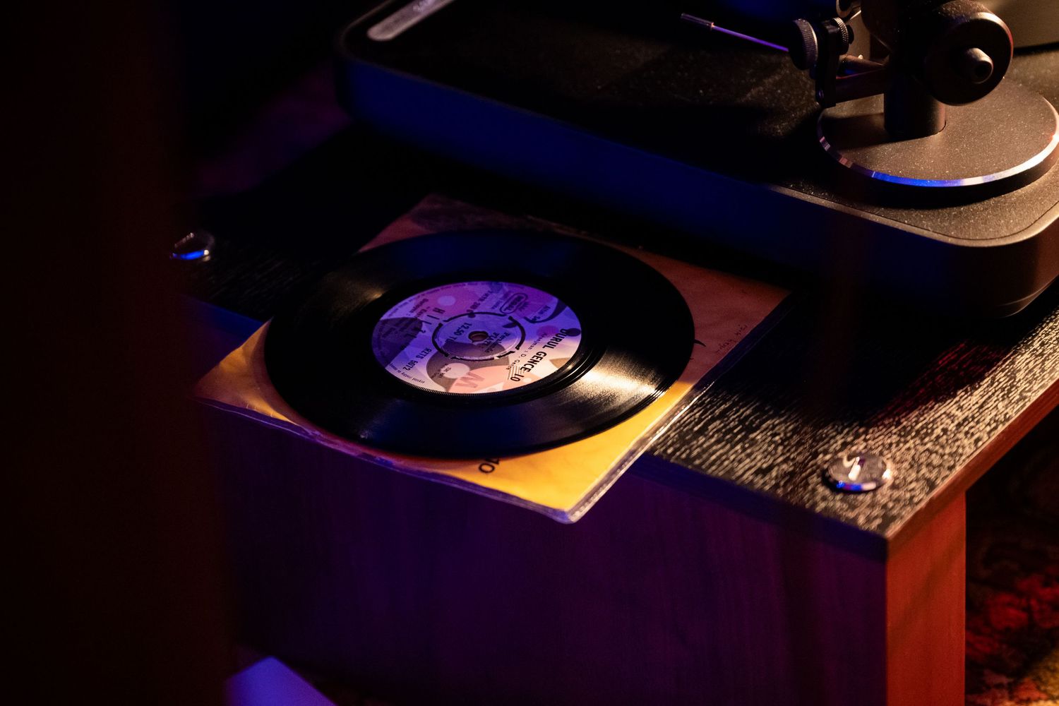 Vinyl record spinning on a turntable with purple lighting in a dark ambient setting.