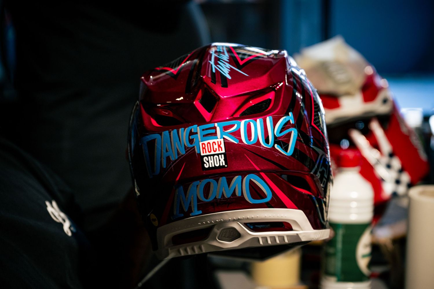 Red motocross helmet with Dangerous and MOMO branding, featuring bold graphic design in blue and white accents.