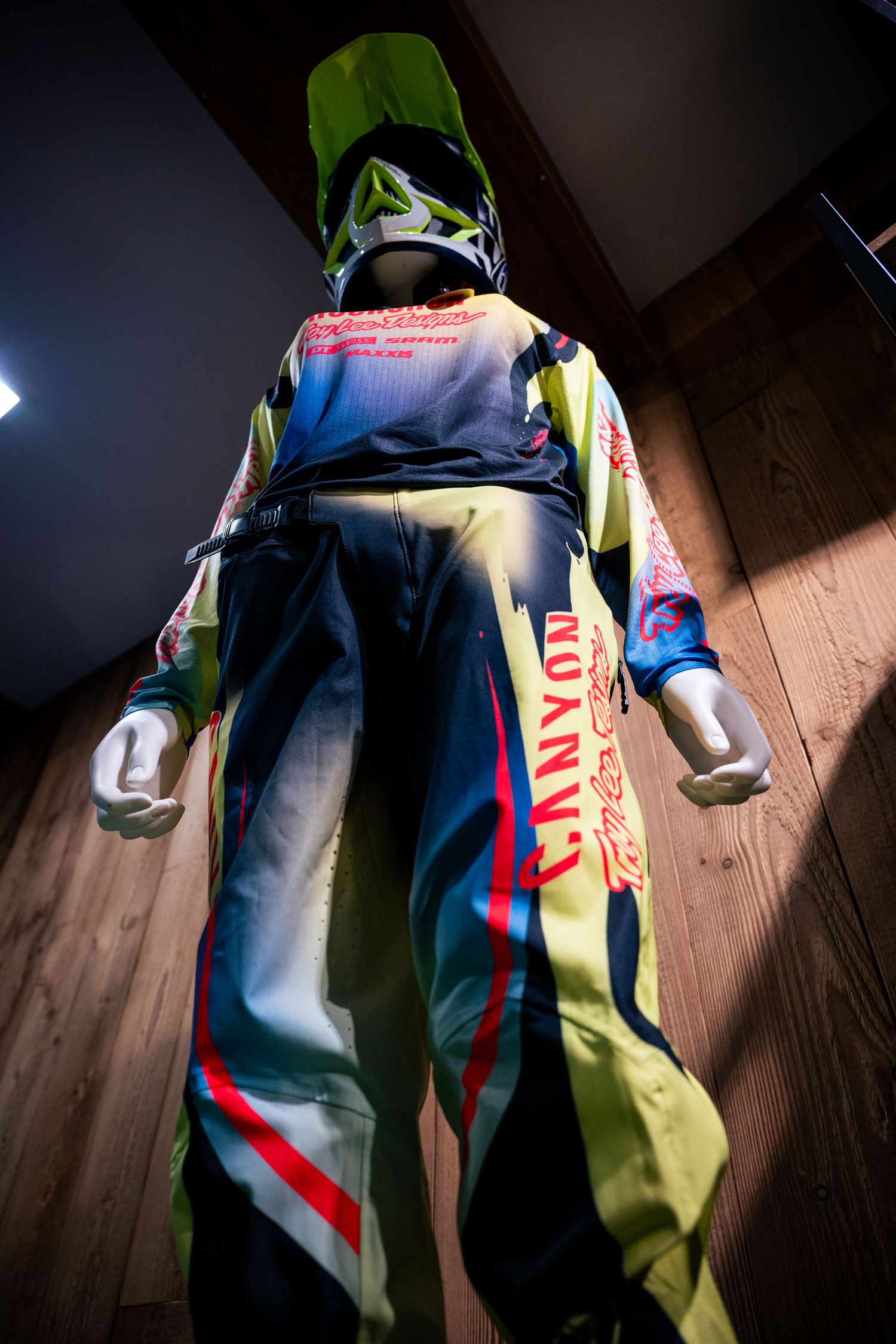 Mannequin wearing Canyon motocross racing suit with neon yellow and blue colors, displayed from behind with helmet.