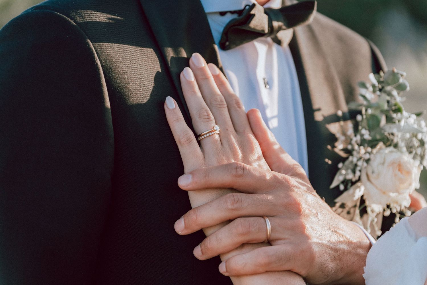 Close-up of bride and groom's hands showing wedding rings with a bridal bouquet in the background.