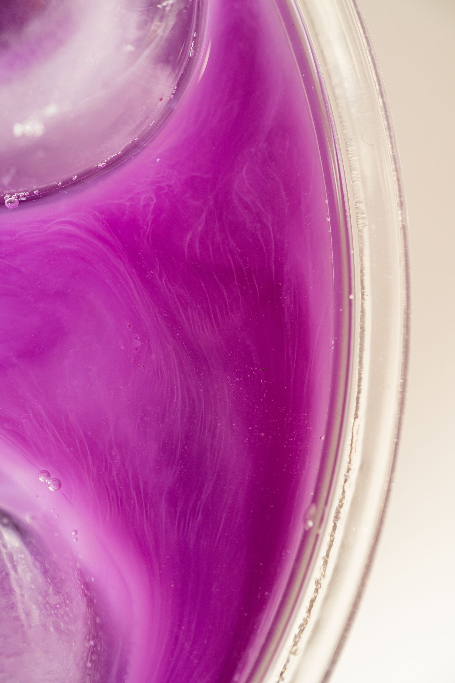 Close-up abstract view of vibrant purple liquid swirling in a clear glass bowl.