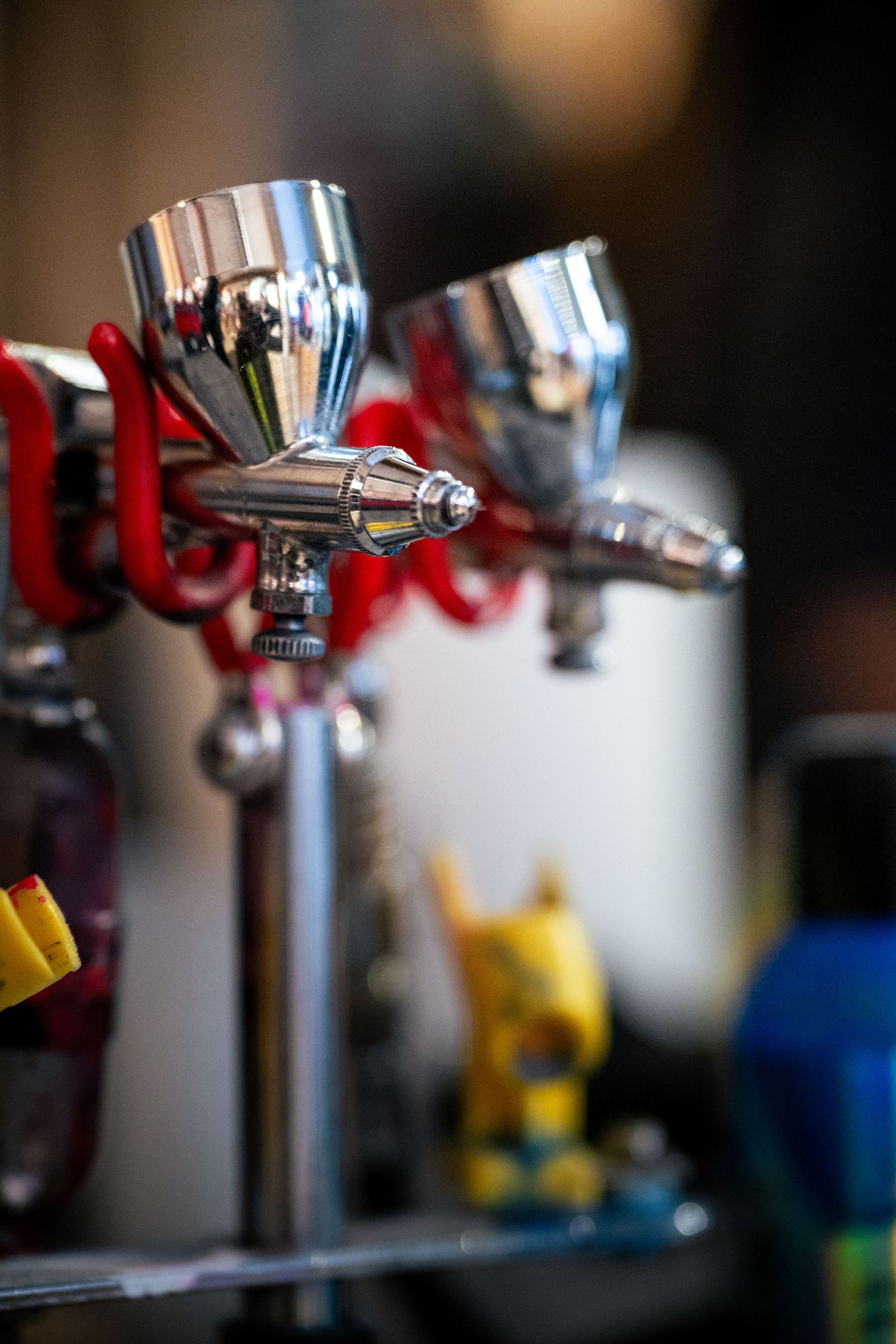 Close-up of two chrome airbrush spray guns mounted on a red stand in a professional workshop setting.