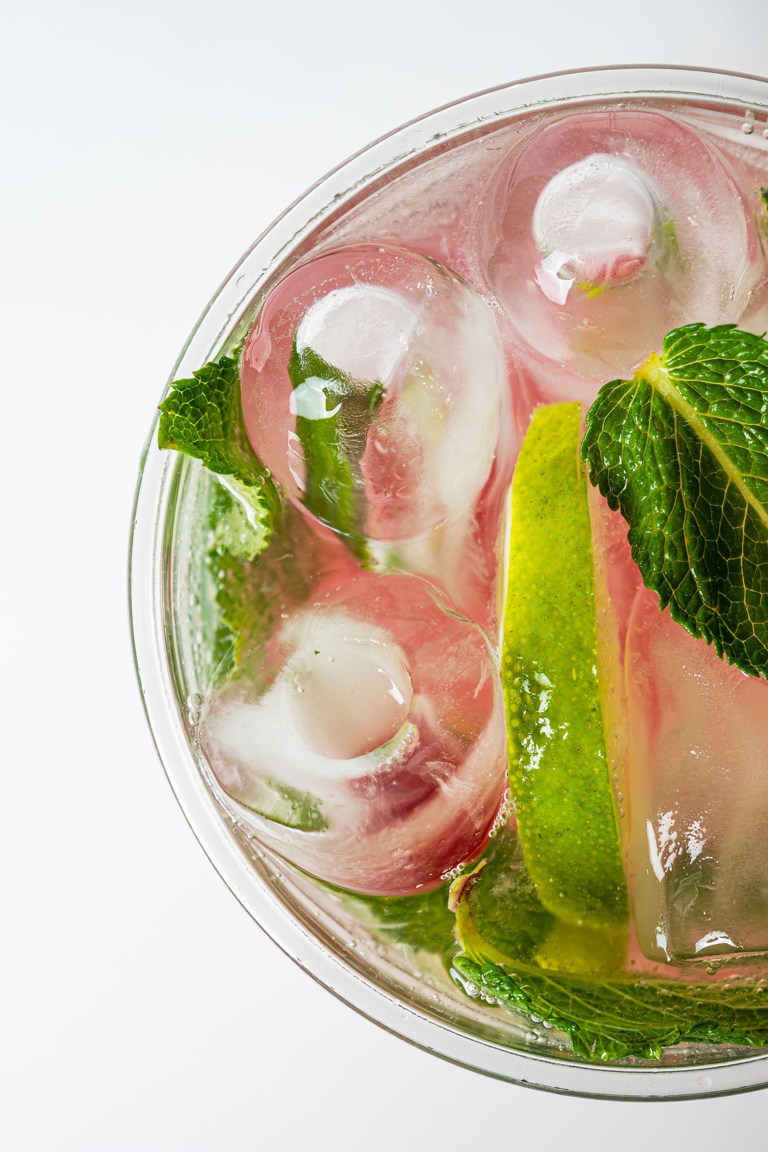 Top view of refreshing pink cocktail with ice cubes, mint leaves, and lime wedge.