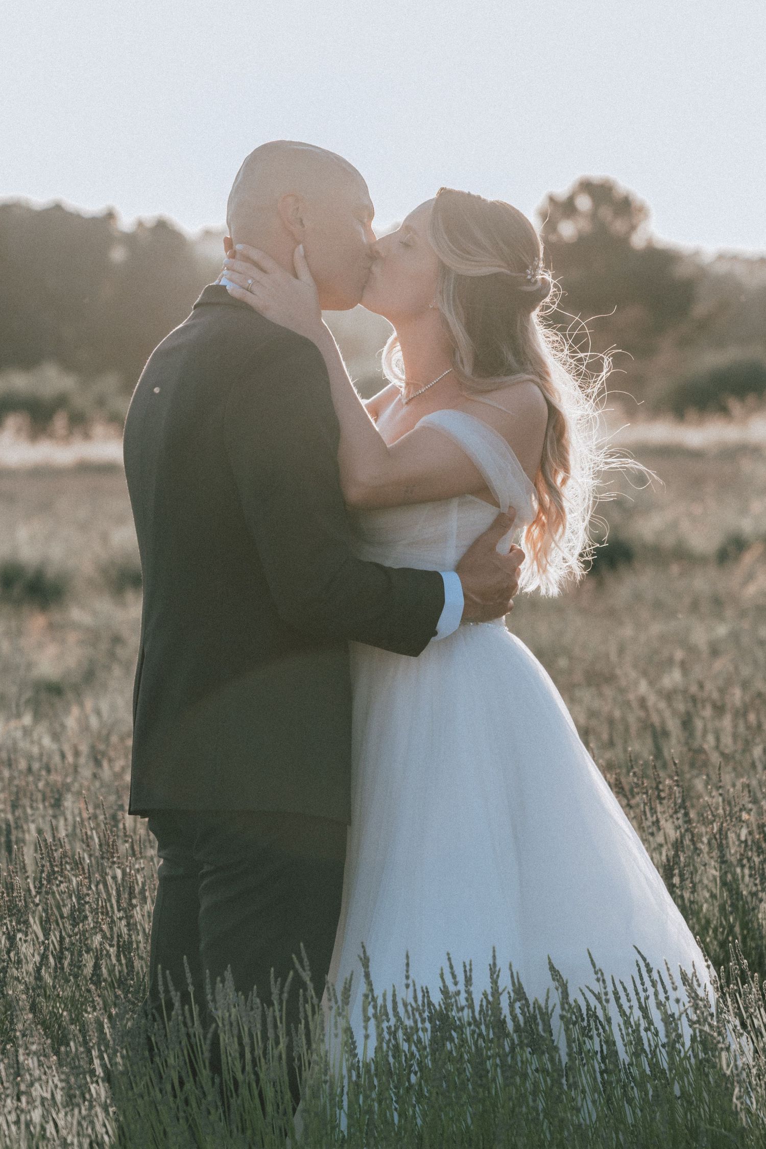 Bride and groom sharing a romantic kiss in a lavender field bathed in golden sunset light.