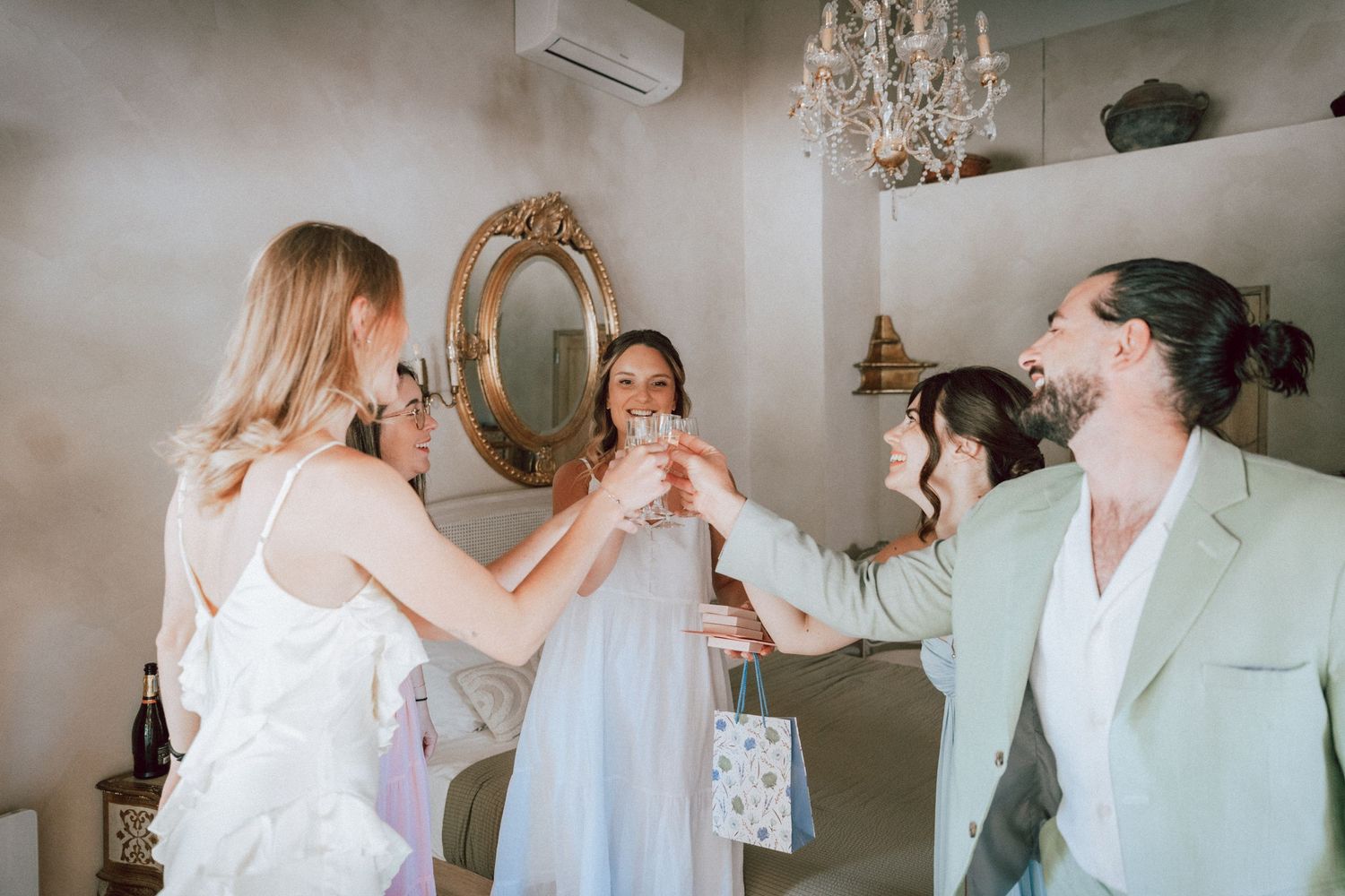 Wedding party guests raising champagne glasses in toast inside elegant room with chandelier.