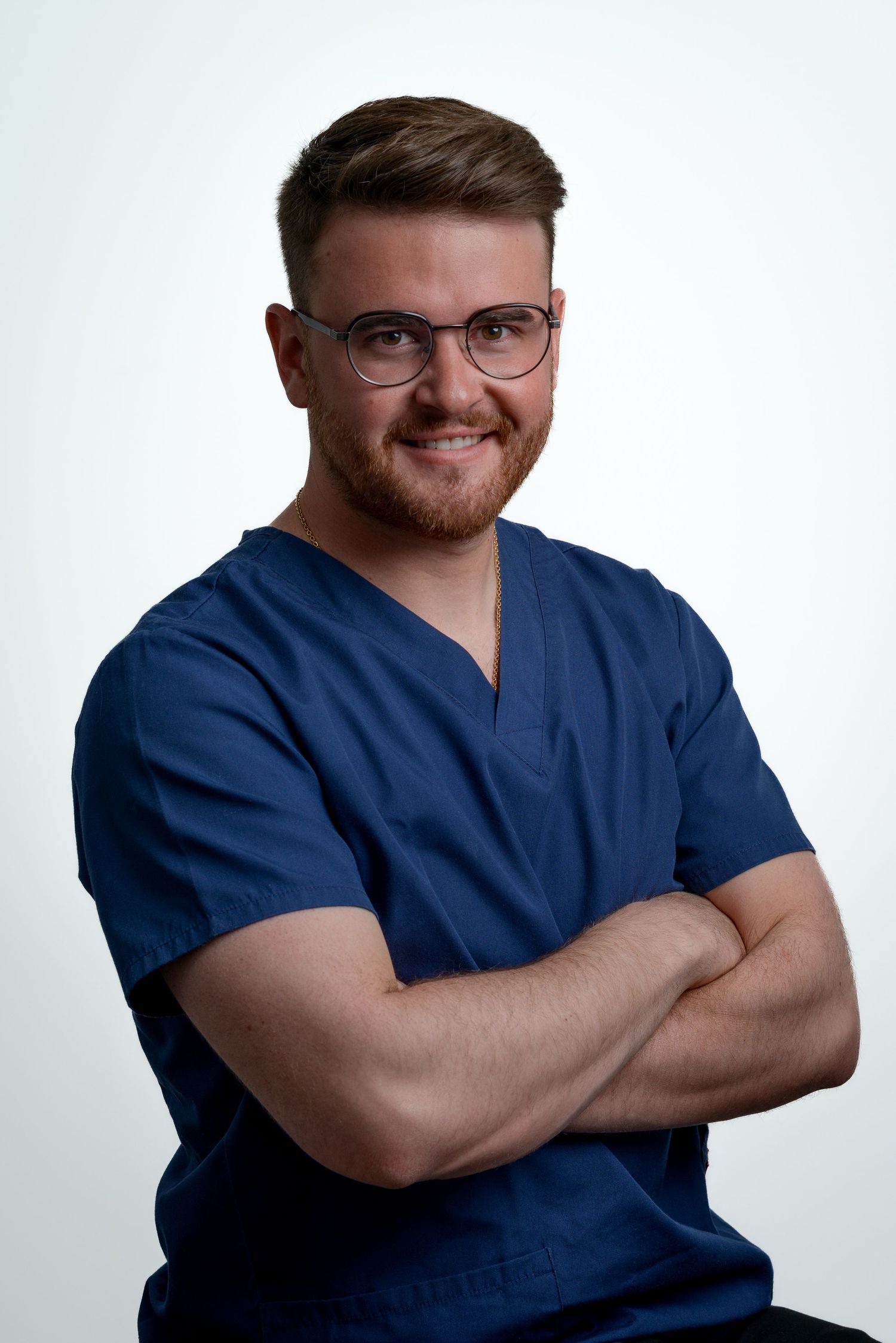 Smiling male healthcare professional in blue scrubs with arms crossed on white background.