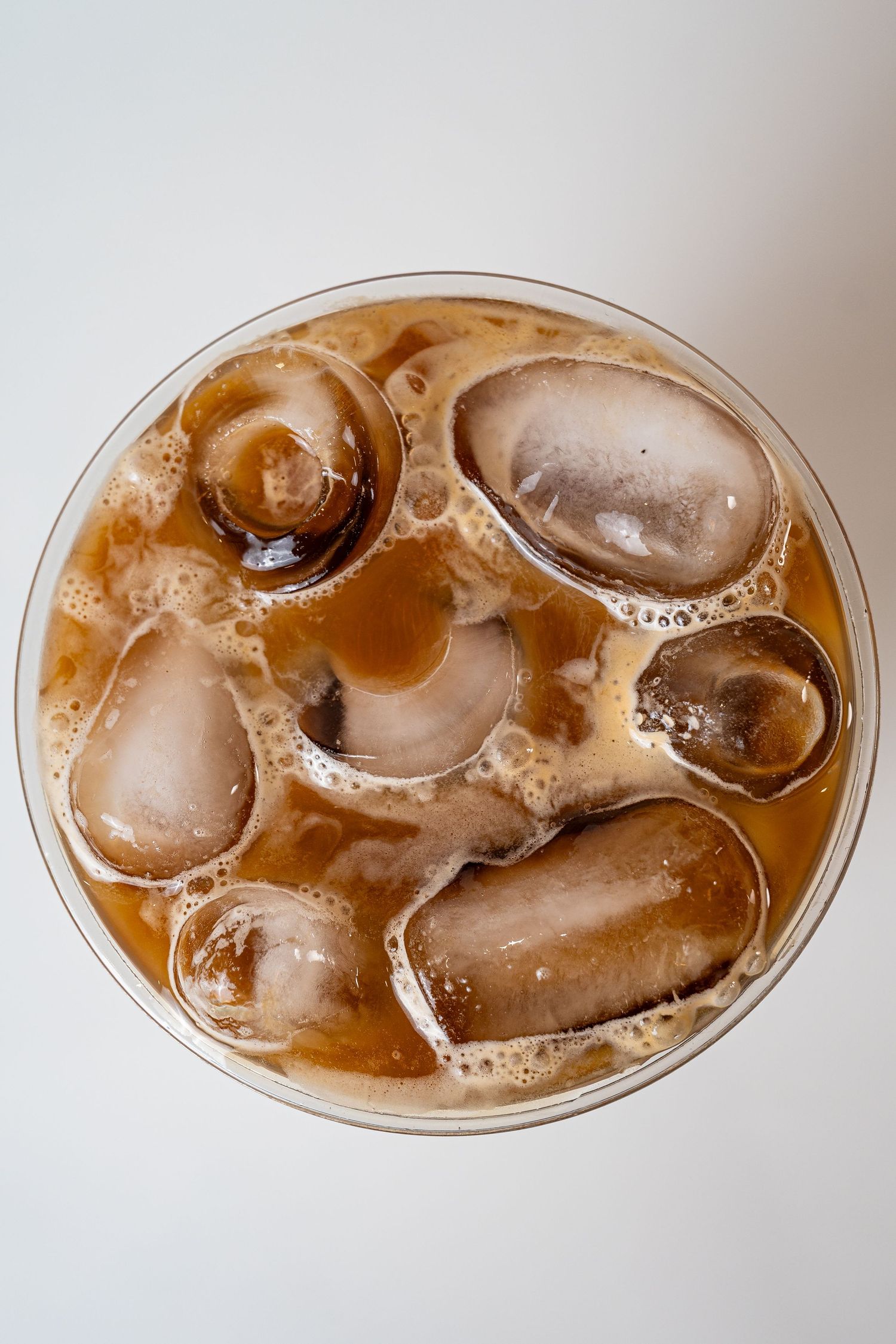 Top-down view of iced coffee with large ice cubes and creamy foam in clear glass.