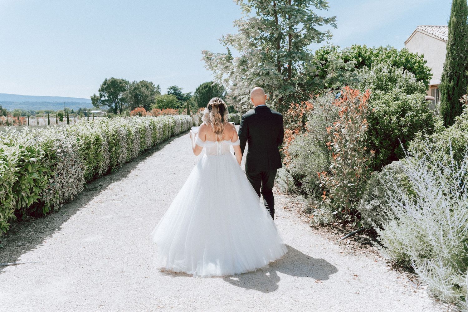 Newlyweds strolling away down garden path surrounded by lush greenery on wedding day.