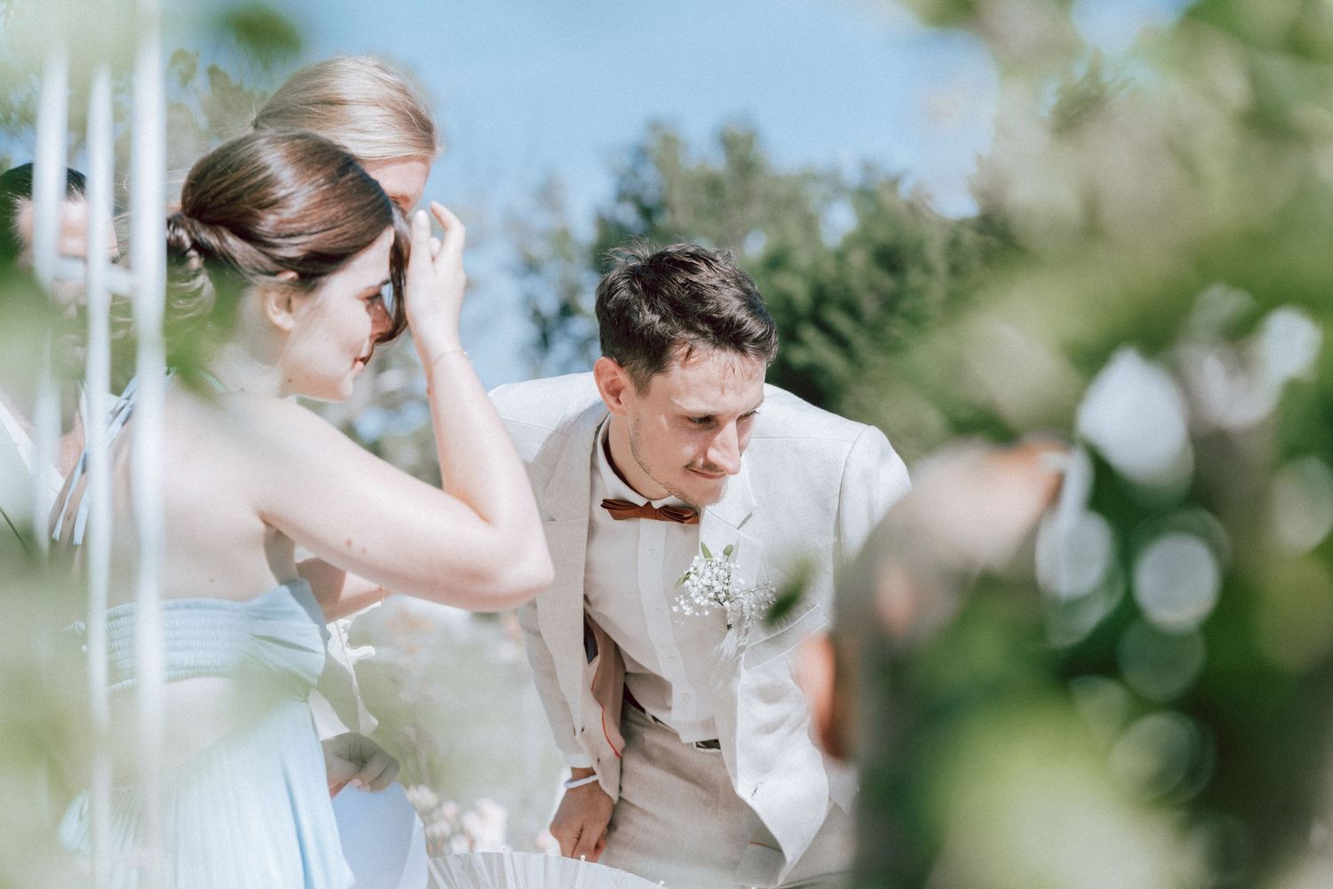 Groom in beige suit leaning forward smiling at bride during outdoor garden wedding ceremony.