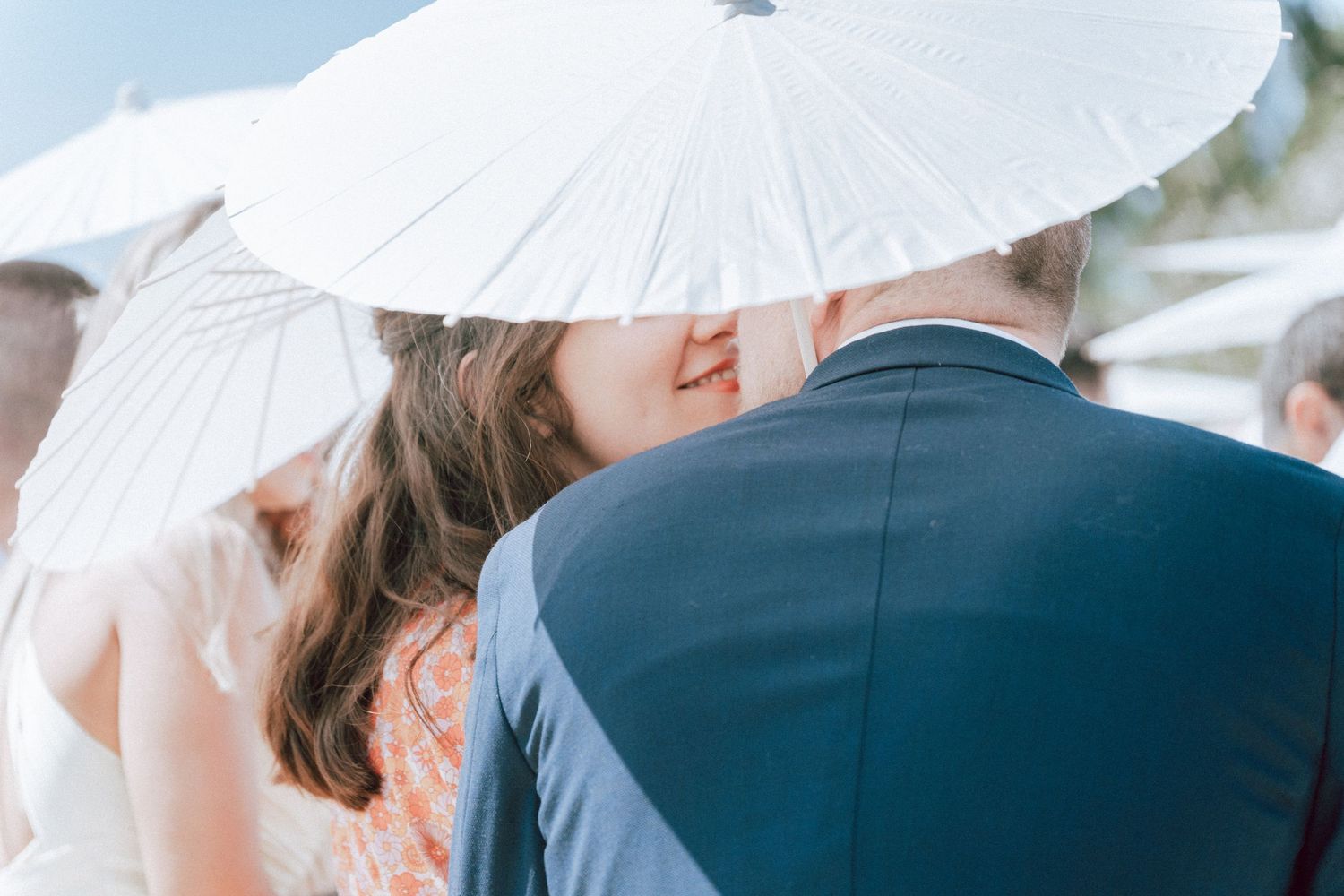 Bride and groom sharing romantic kiss under white parasol umbrella at outdoor wedding.