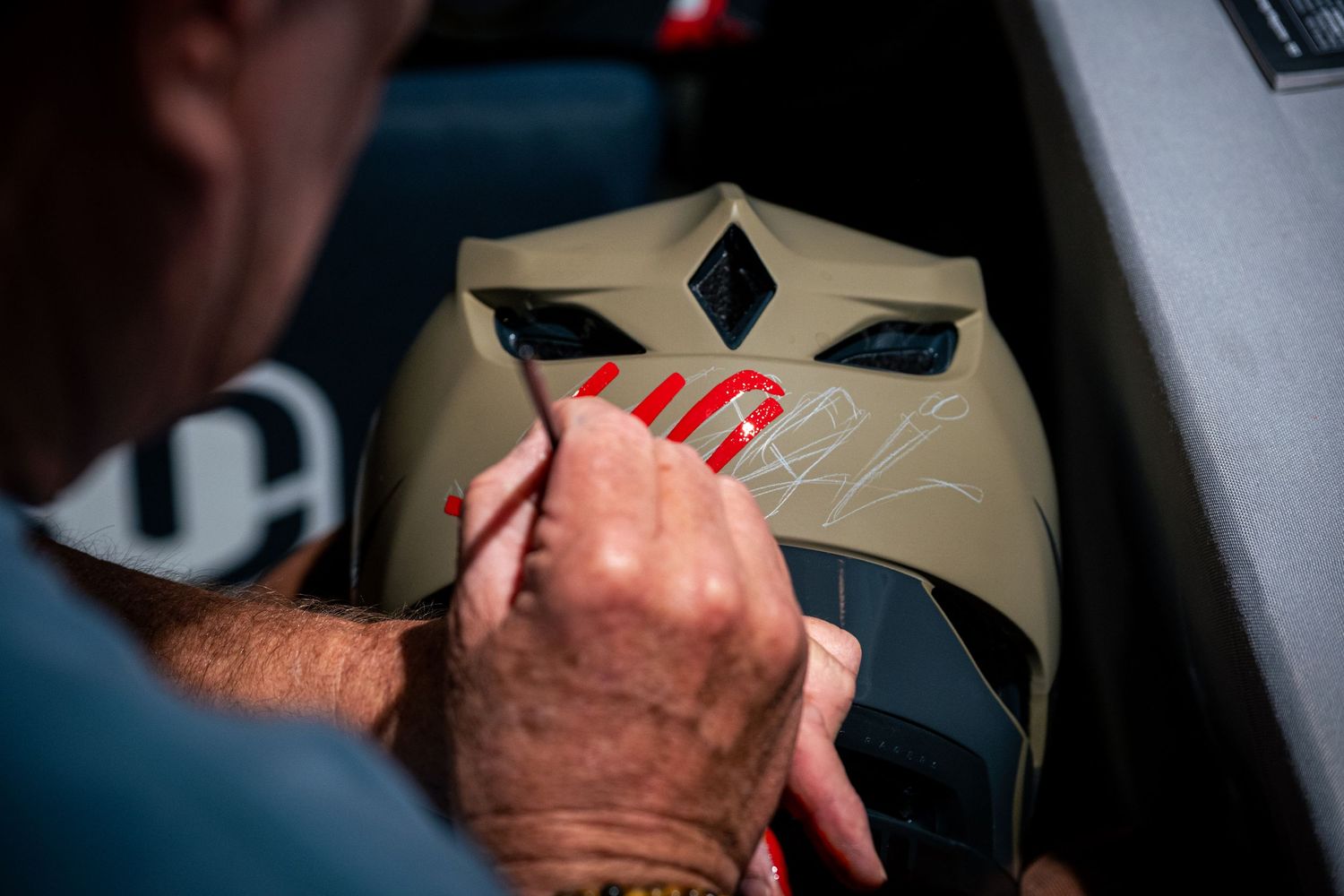 Artist signing a tan motocross helmet with a silver marker up close.