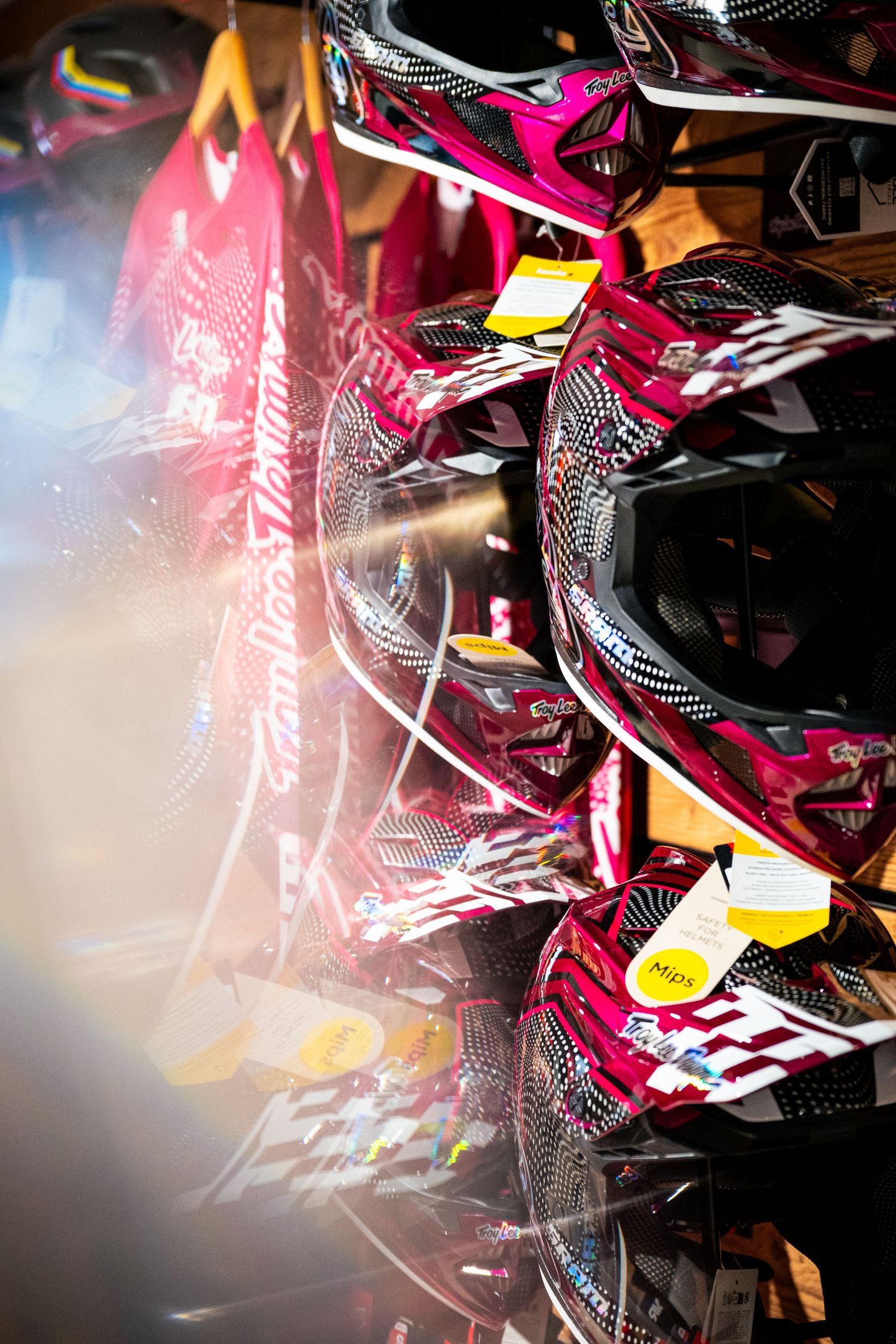 Pink and black motorcycle helmets displayed on a rack in a retail store with price tags attached.