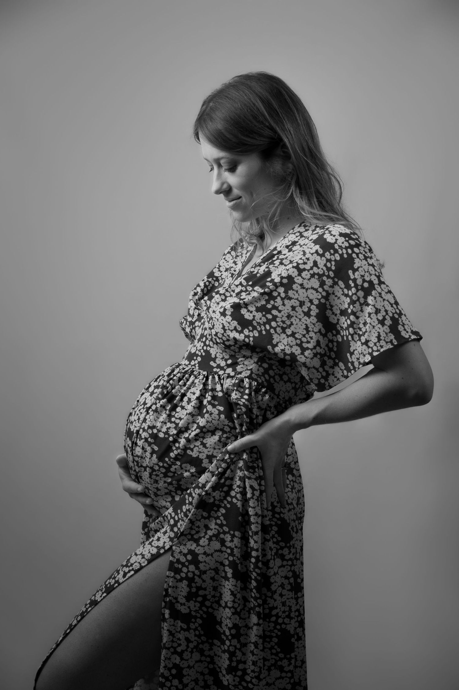 Black and white photo of a pregnant woman in a floral dress gently cradling her baby bump.