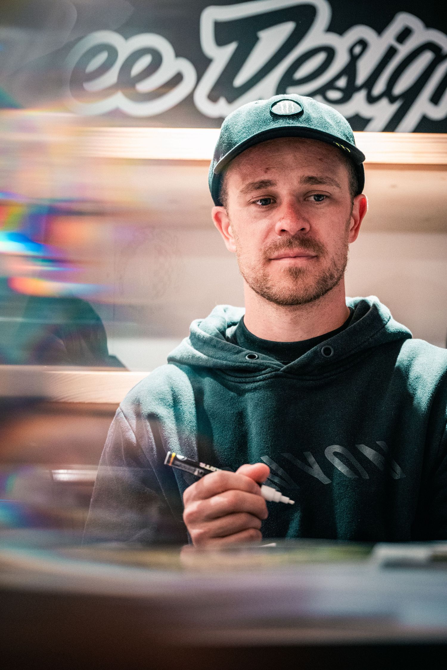 Man in green hoodie and cap holds a pen at Troy Lee Designs store, captured with artistic light streaks.