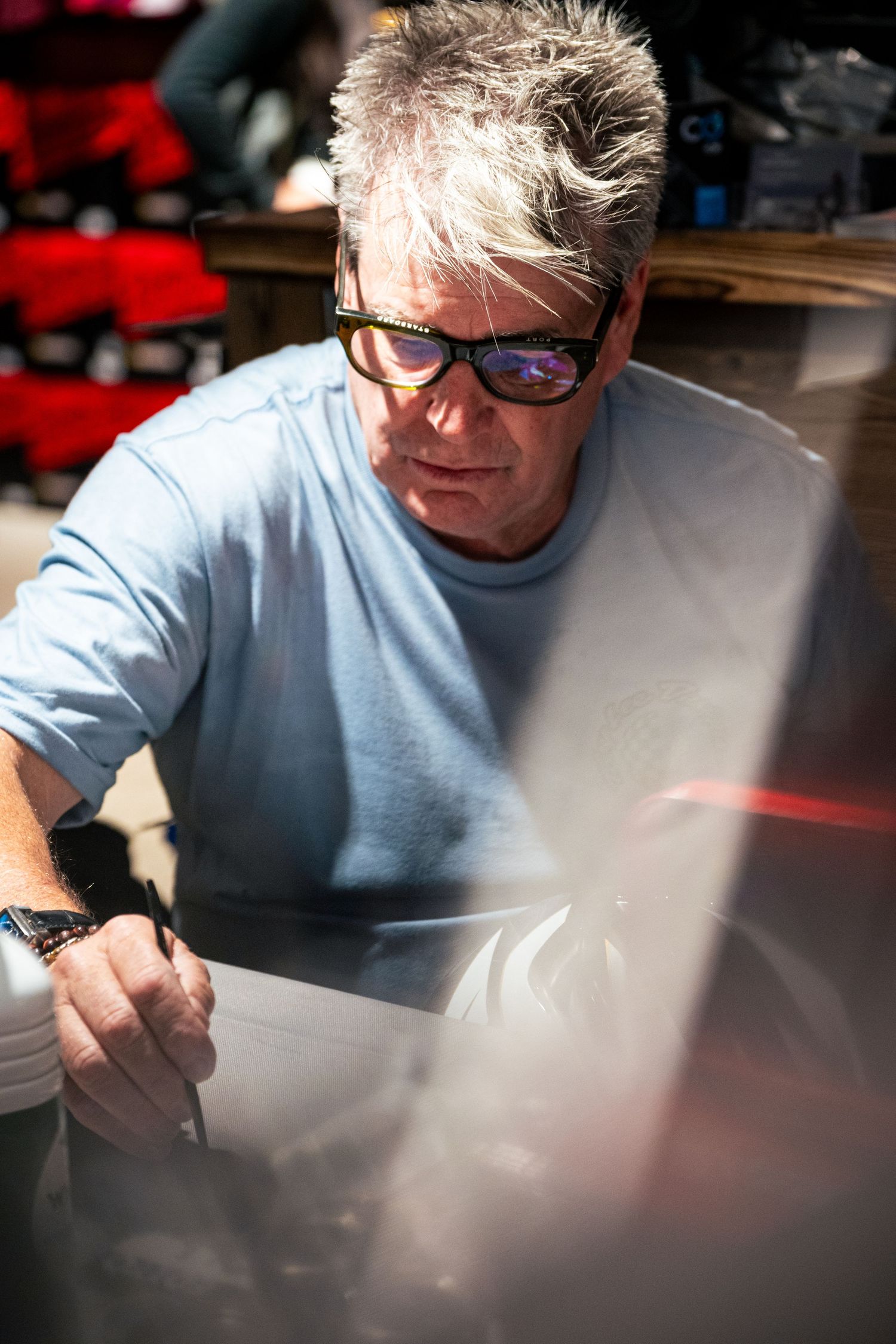 Middle-aged man with gray hair and black glasses examines documents outdoors in bright sunlight.