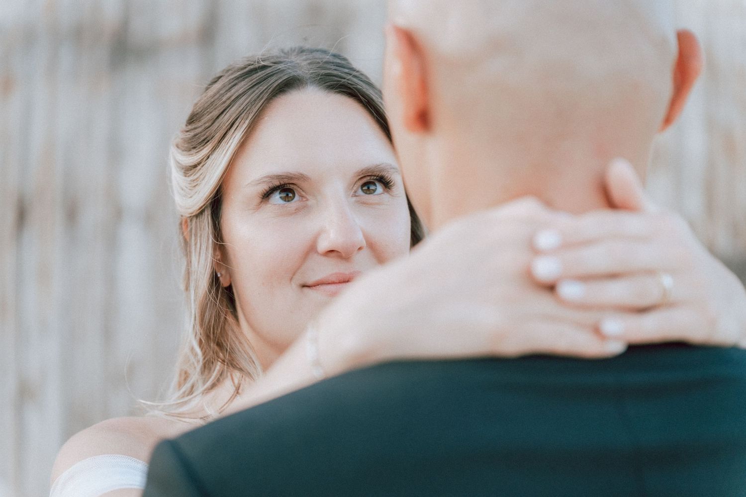 Bride gazing lovingly at groom with diamond ring visible during romantic wedding dance.