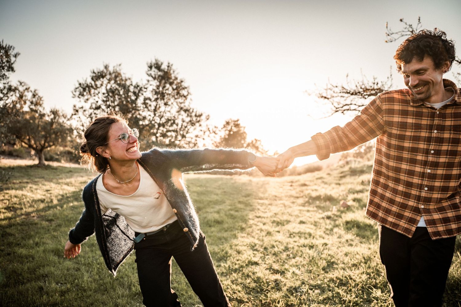 Joyful couple holding hands running through a sunlit field at golden hour.