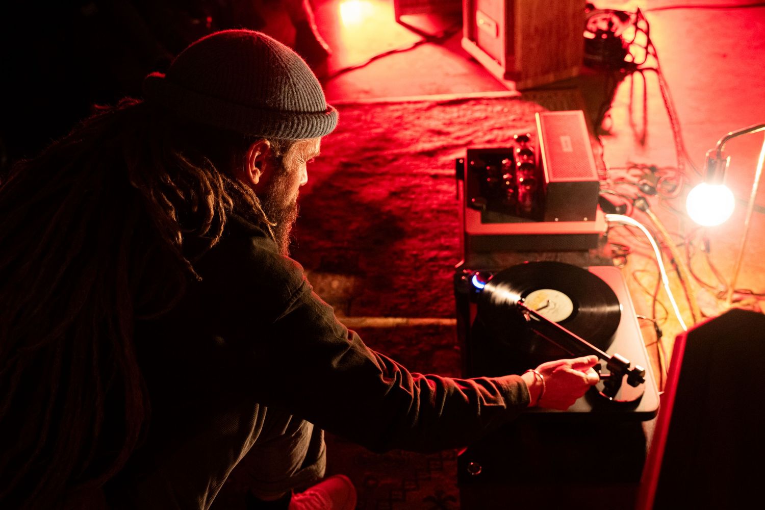 DJ operating vinyl turntable equipment under warm red lighting at a music event.