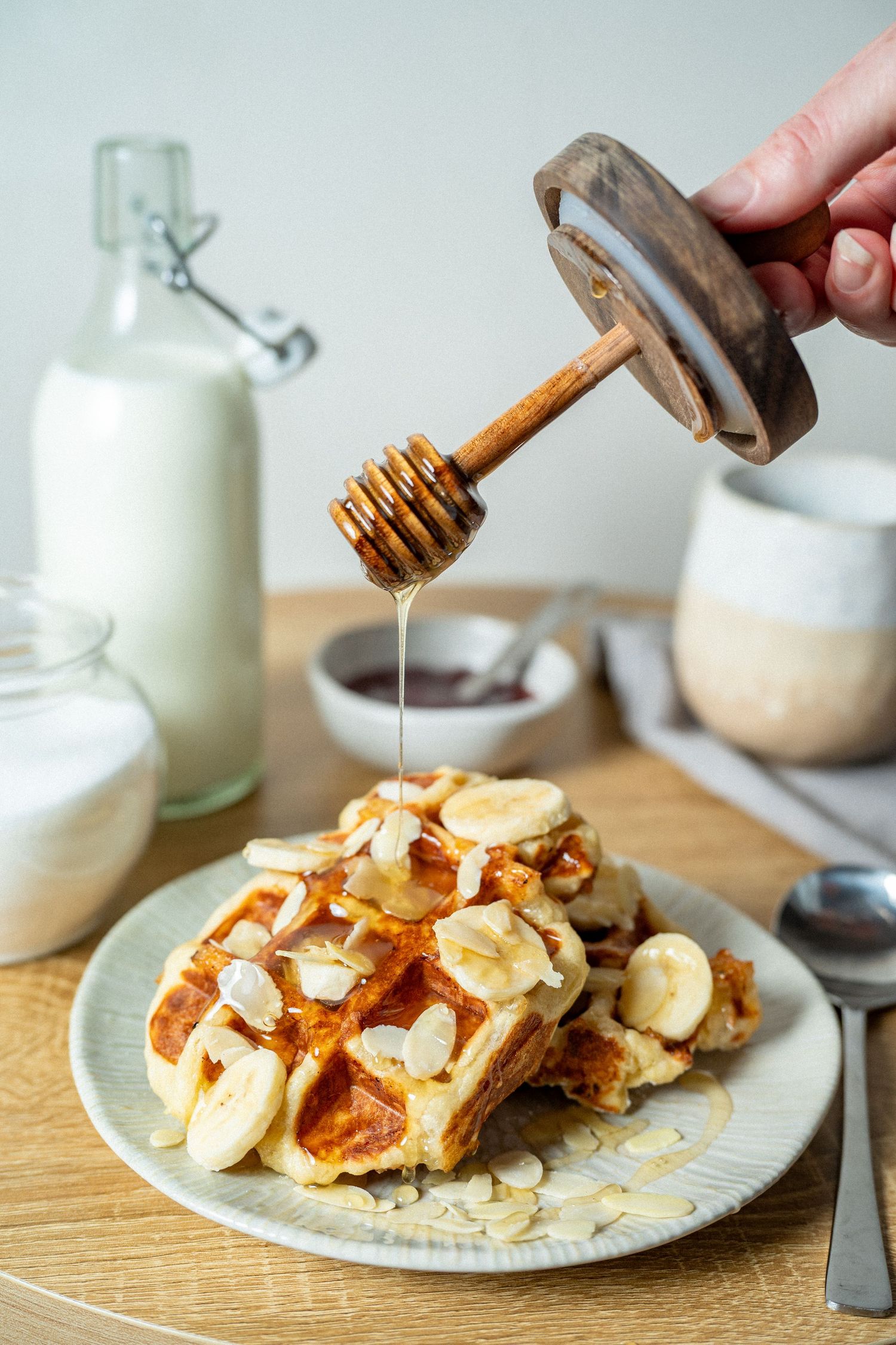 Honey being drizzled from a wooden dipper onto banana almond waffles on a plate.