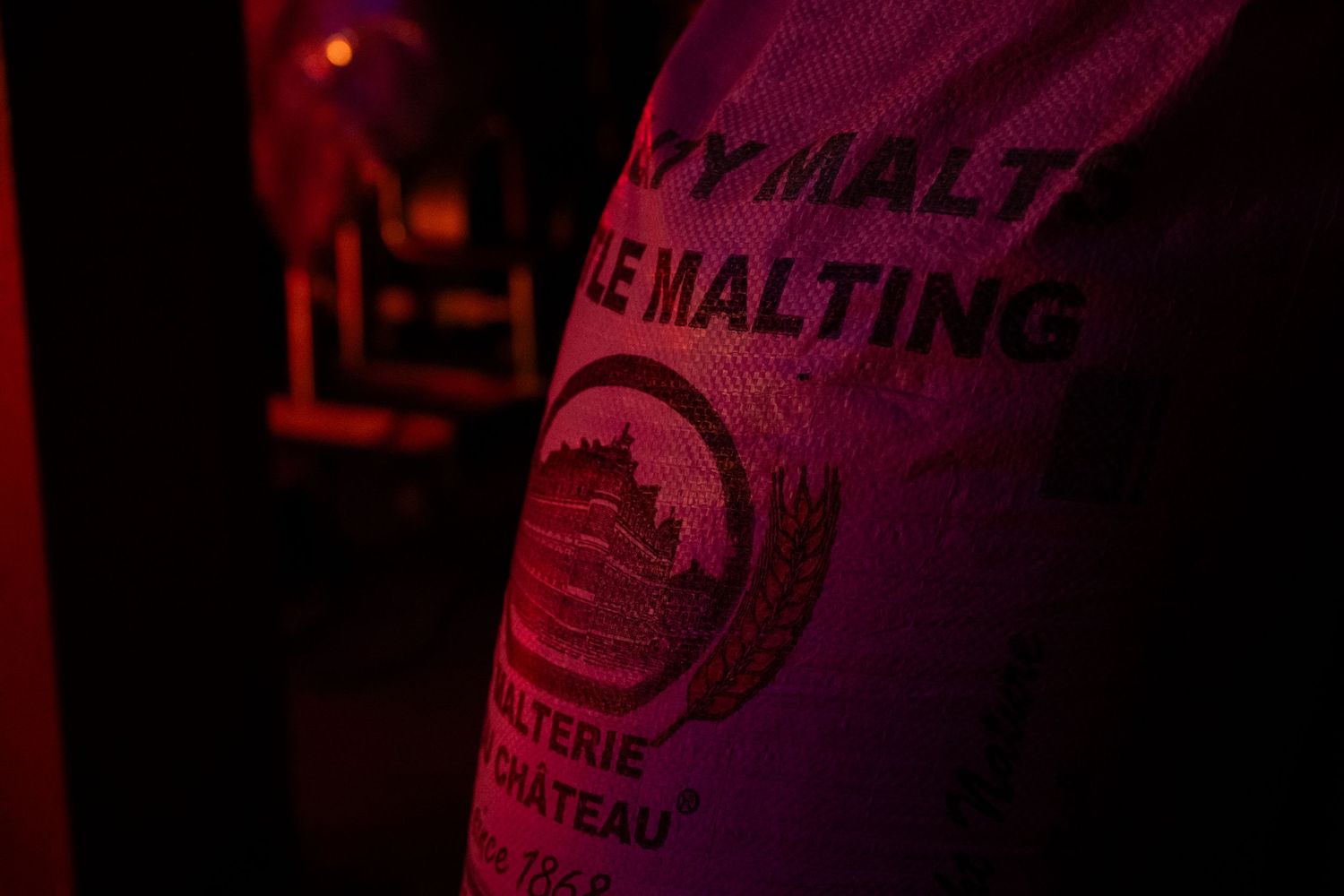 Close-up of a malting grain sack labeled Le Malting, illuminated by red light in a brewery setting.