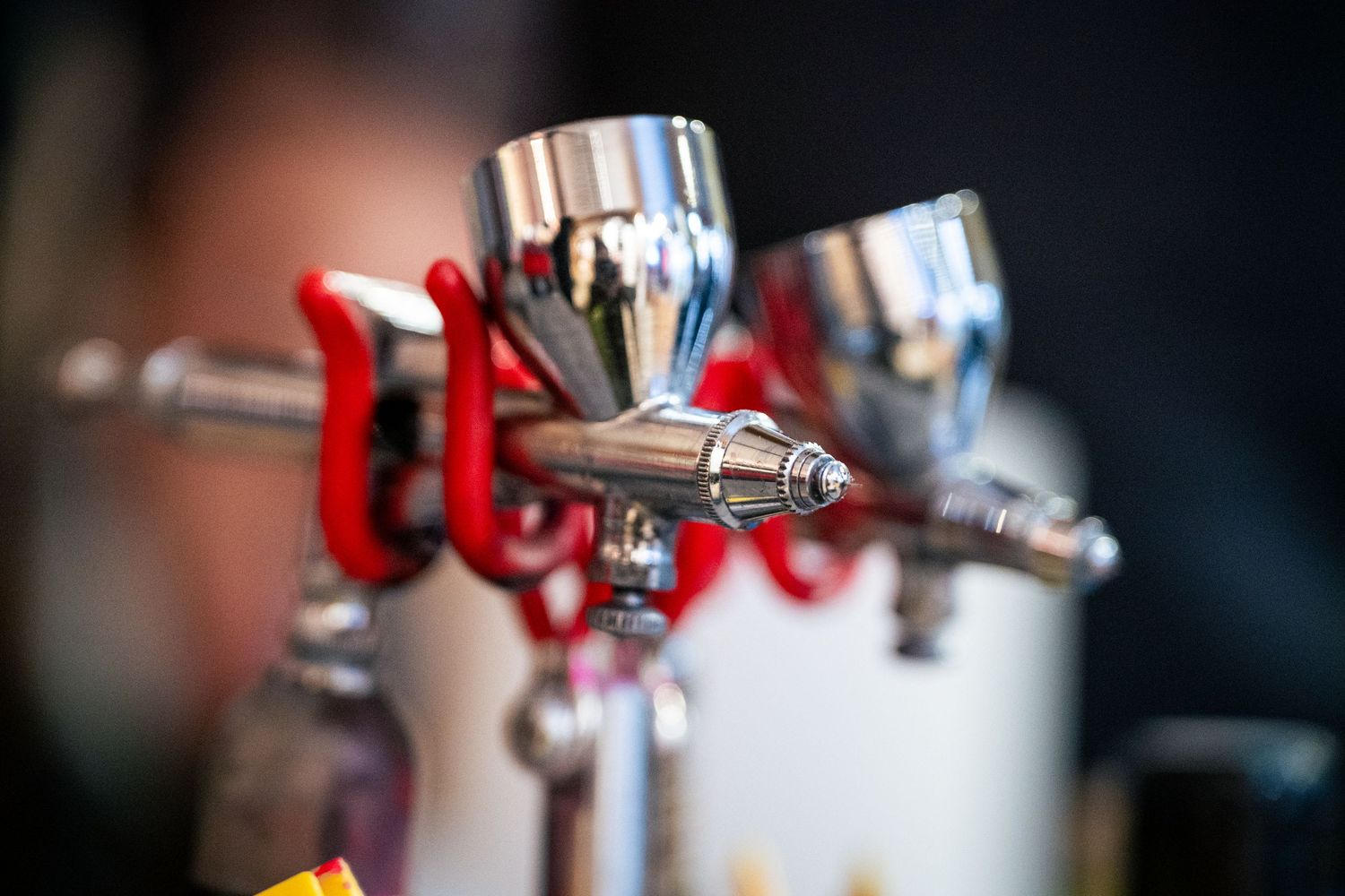 Three chrome airbrush spray guns mounted on a stand for custom helmet painting.
