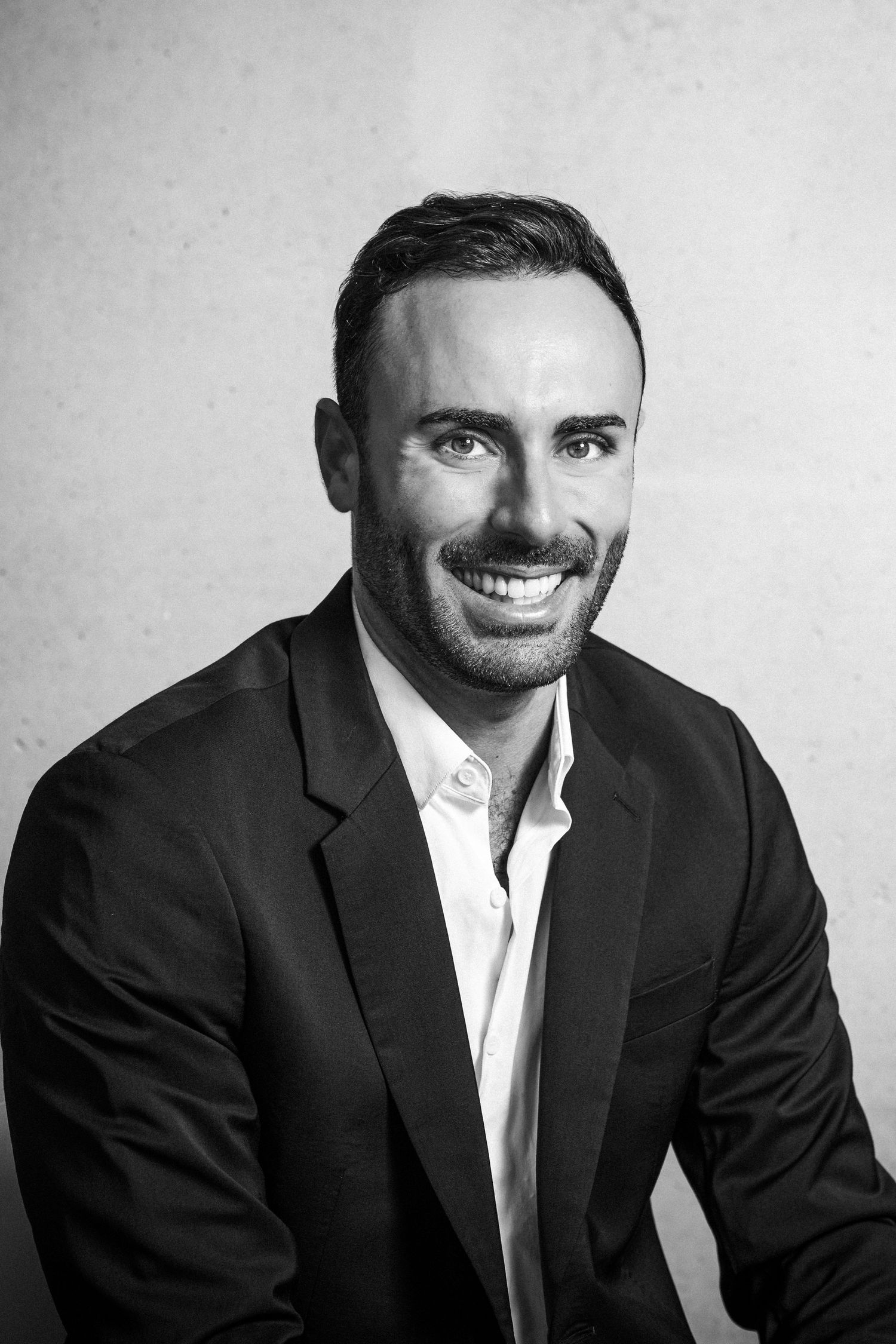 Smiling professional man in black suit jacket photographed in black and white portrait.