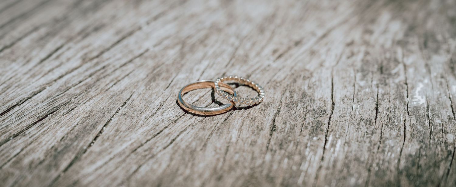 Two delicate gold wedding bands resting on a rustic weathered wooden surface.