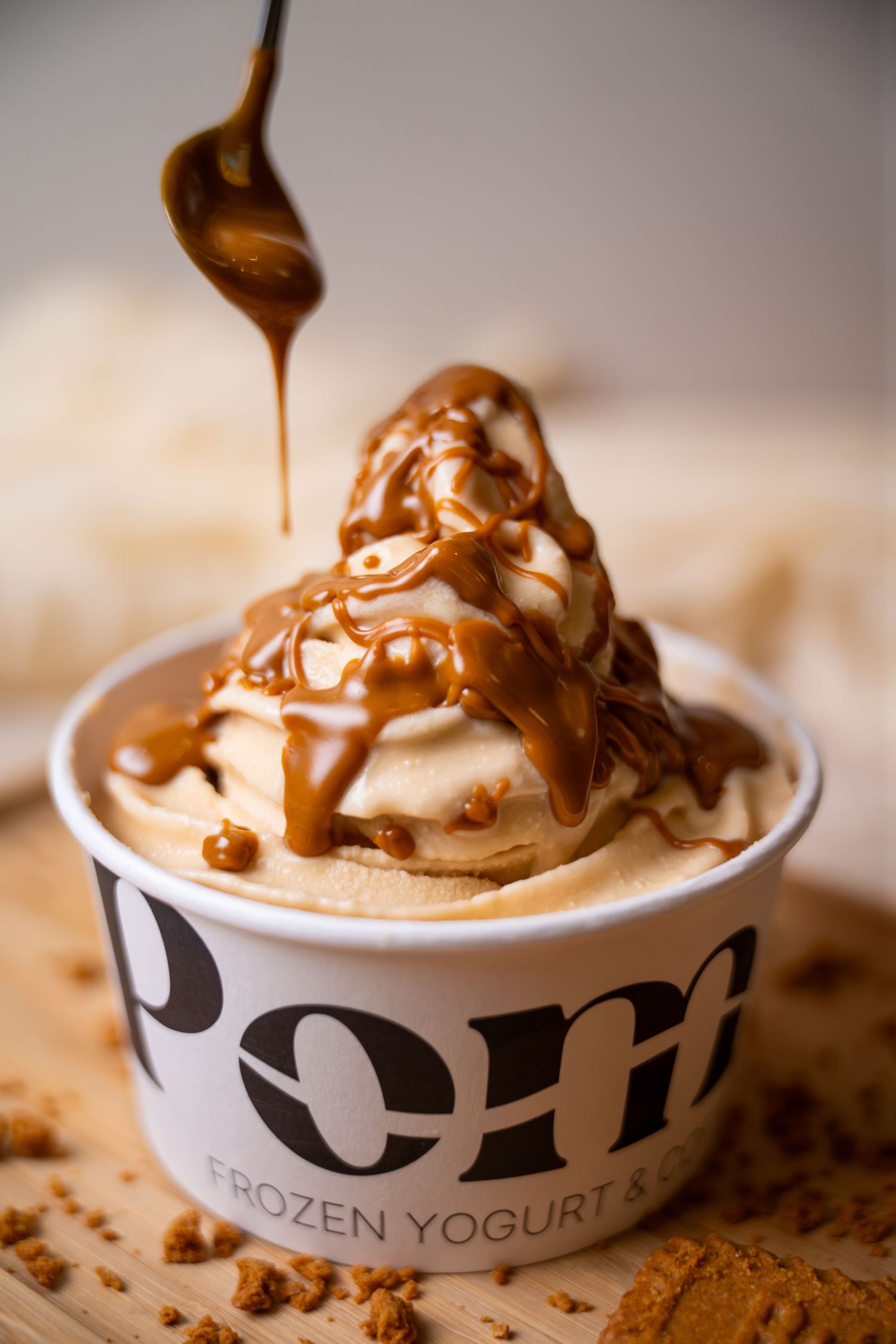 Caramel sauce drizzled over frozen yogurt in a Pom Frozen Yogurt cup on a wooden surface.