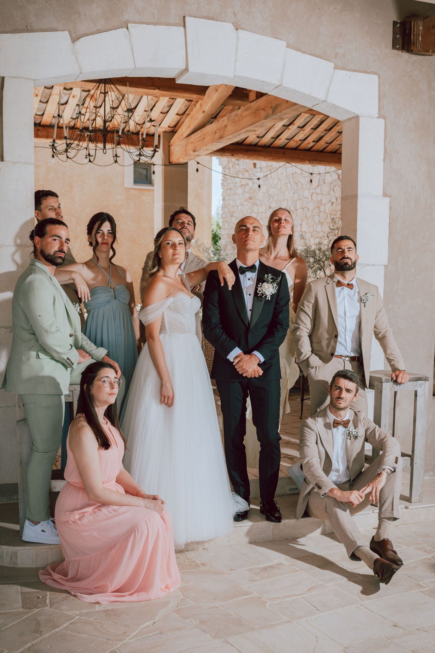 Wedding party posing together under stone arch at elegant venue with chandelier.