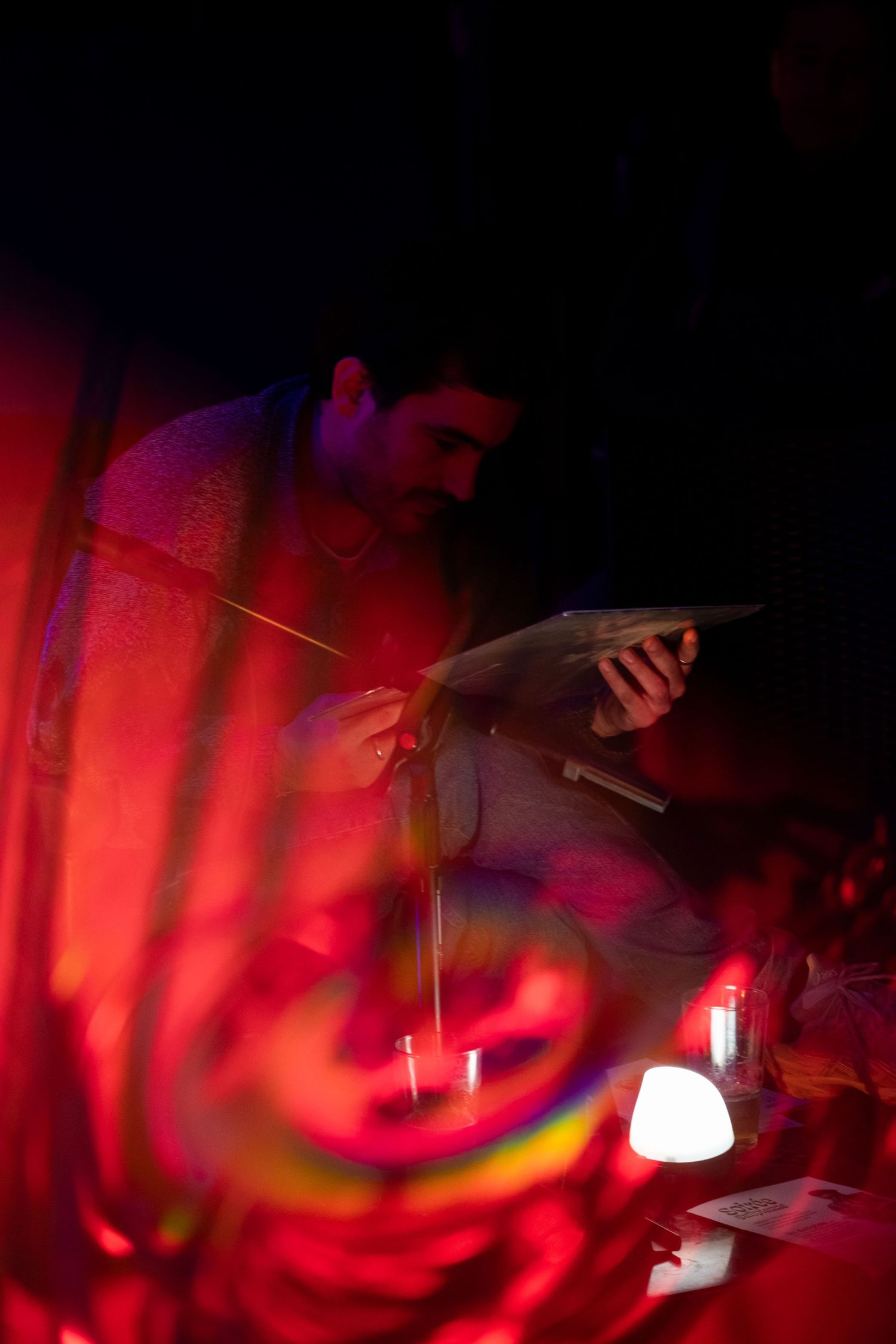 Man examining object under dramatic red lighting in dark atmospheric setting with candles.