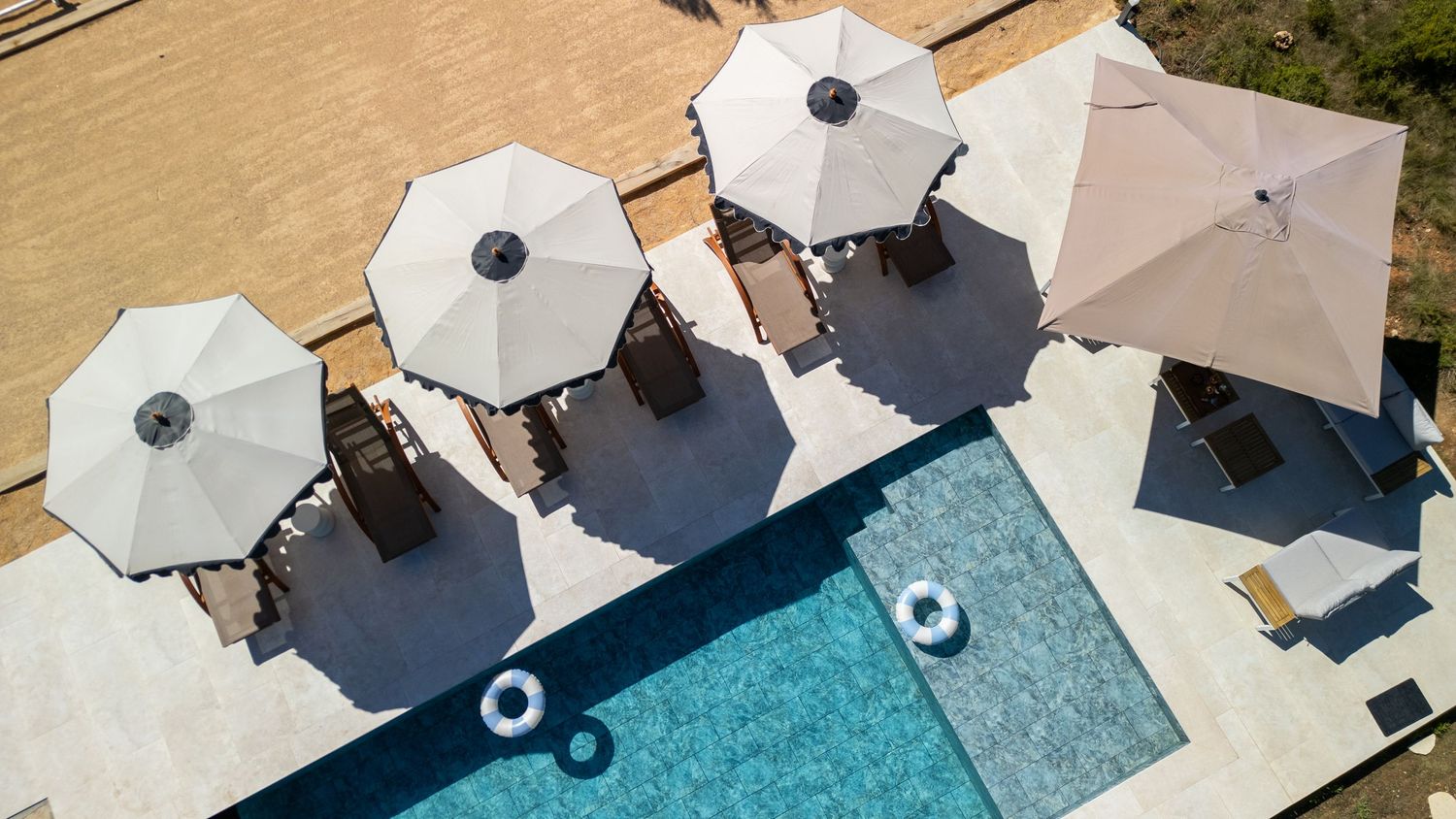 Aerial view of a luxury pool area with white umbrellas, lounge chairs, and a blue swimming pool with float rings.