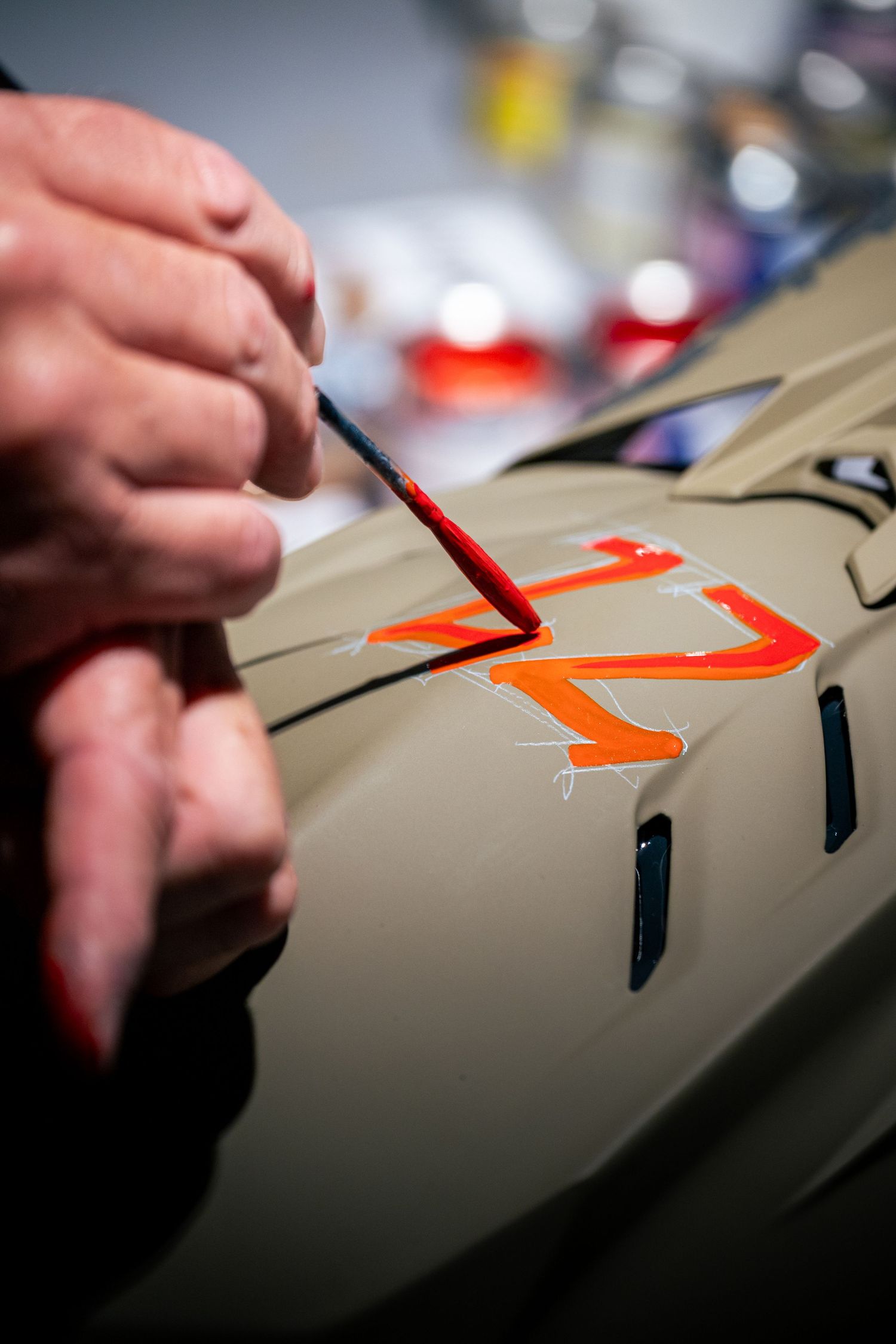 Artist hand-painting orange number on a tan motocross helmet with a fine brush.