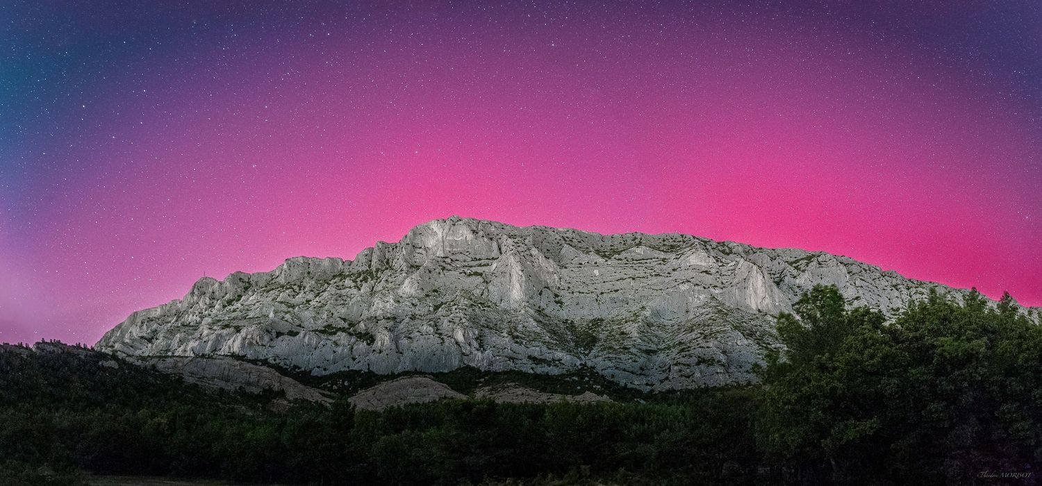 Dramatic pink and purple aurora borealis illuminating rocky mountain cliff against starry night sky.