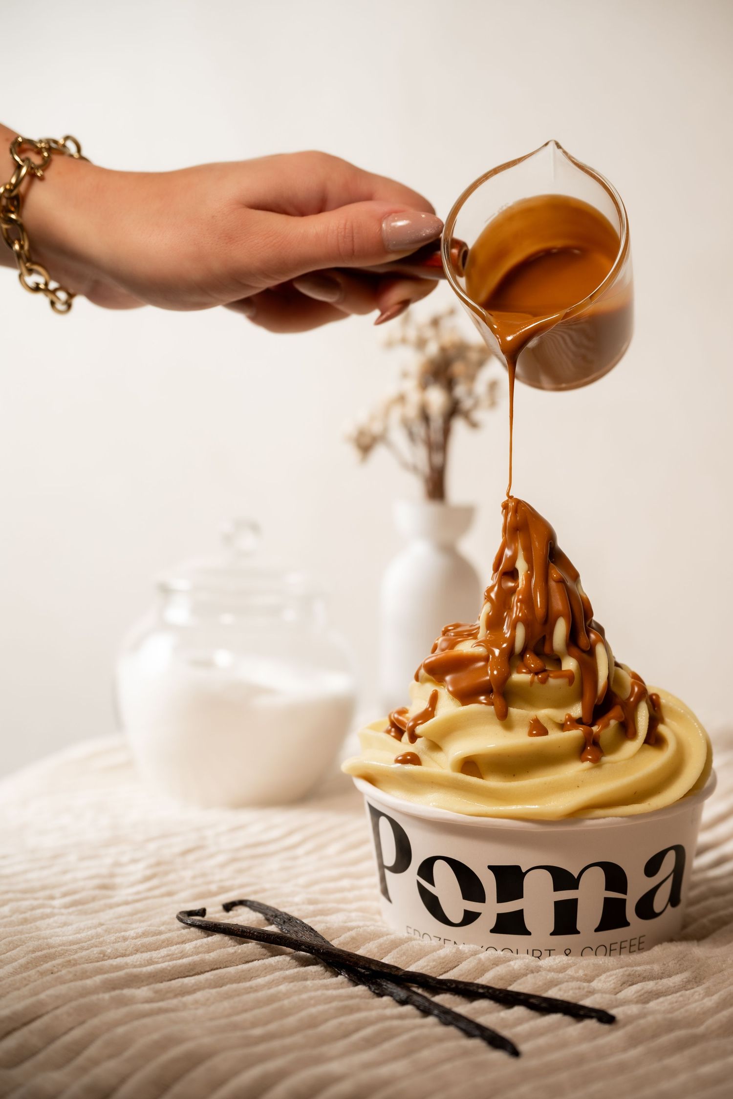 Hand pouring caramel sauce over a swirled ice cream dessert in a Poma branded cup.