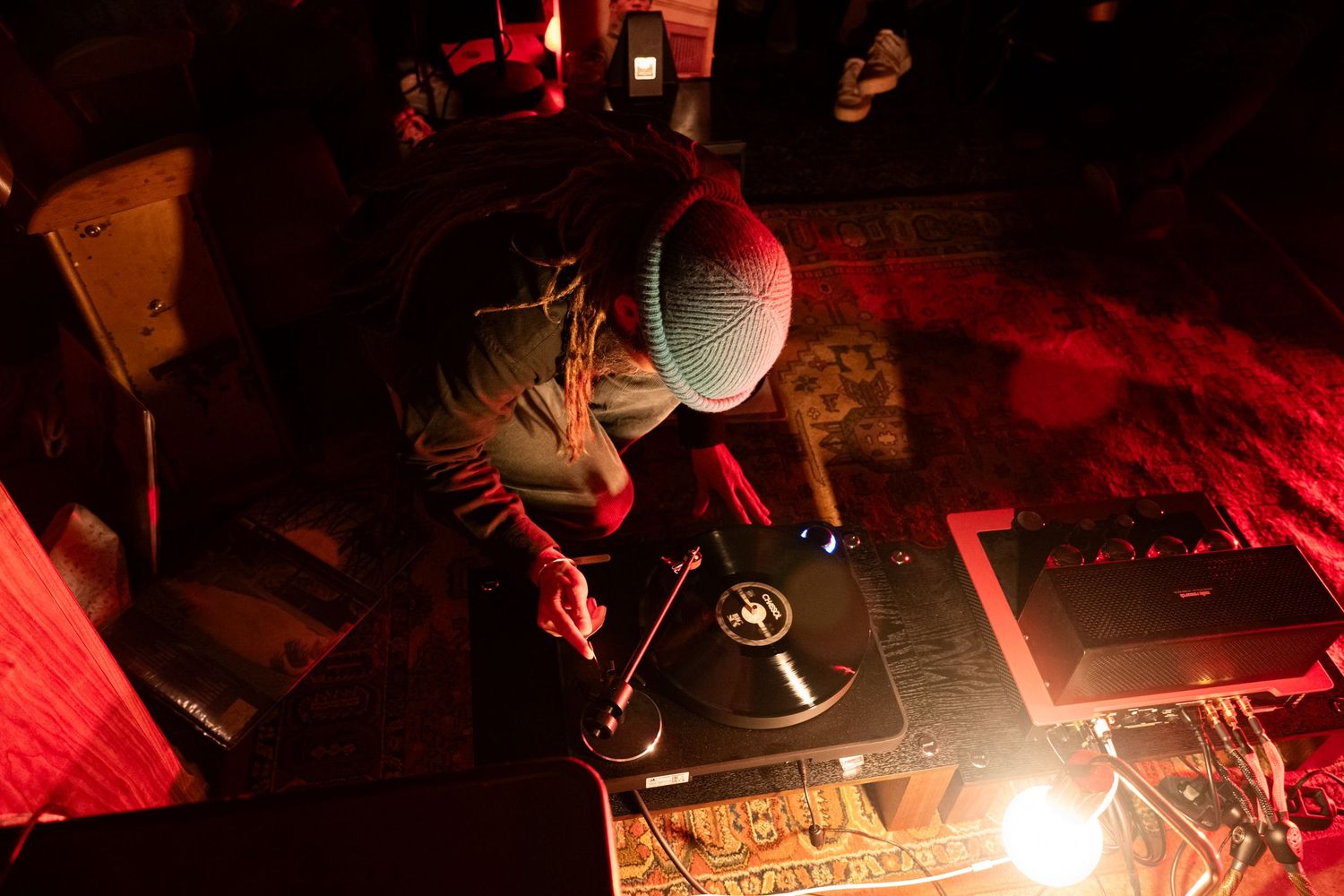 DJ spinning vinyl records on turntables under red lighting at a nighttime music event.